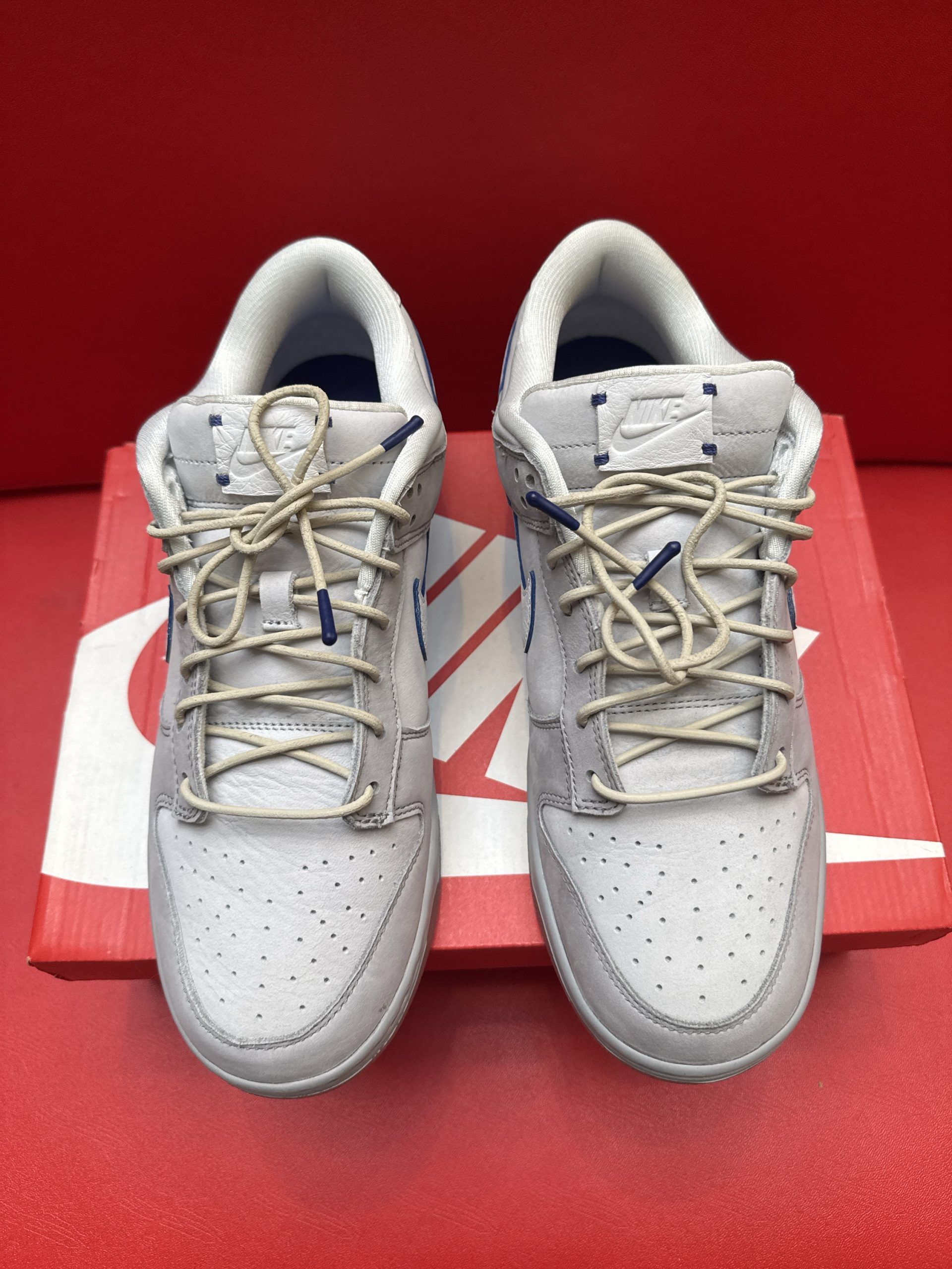 Grey Nike Dunk Low sneaker, sole, and red box on a red surface.