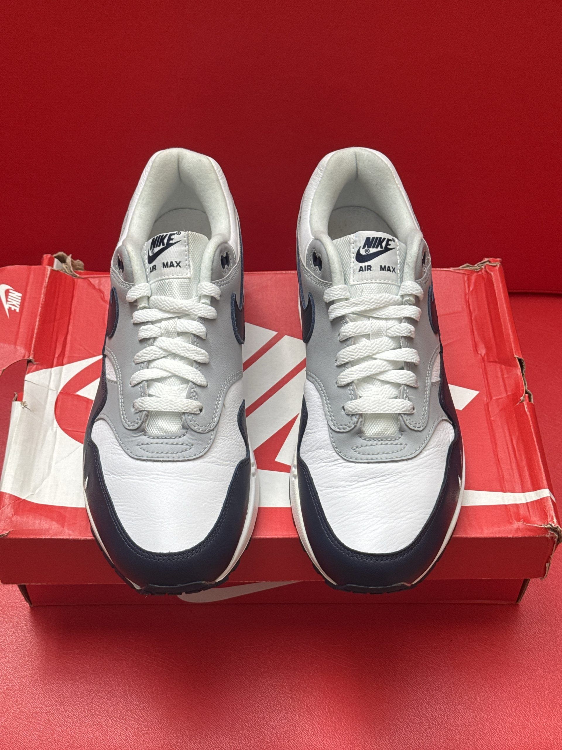 Nike Air Max 1 sneakers in gray, navy, and white on a red box.