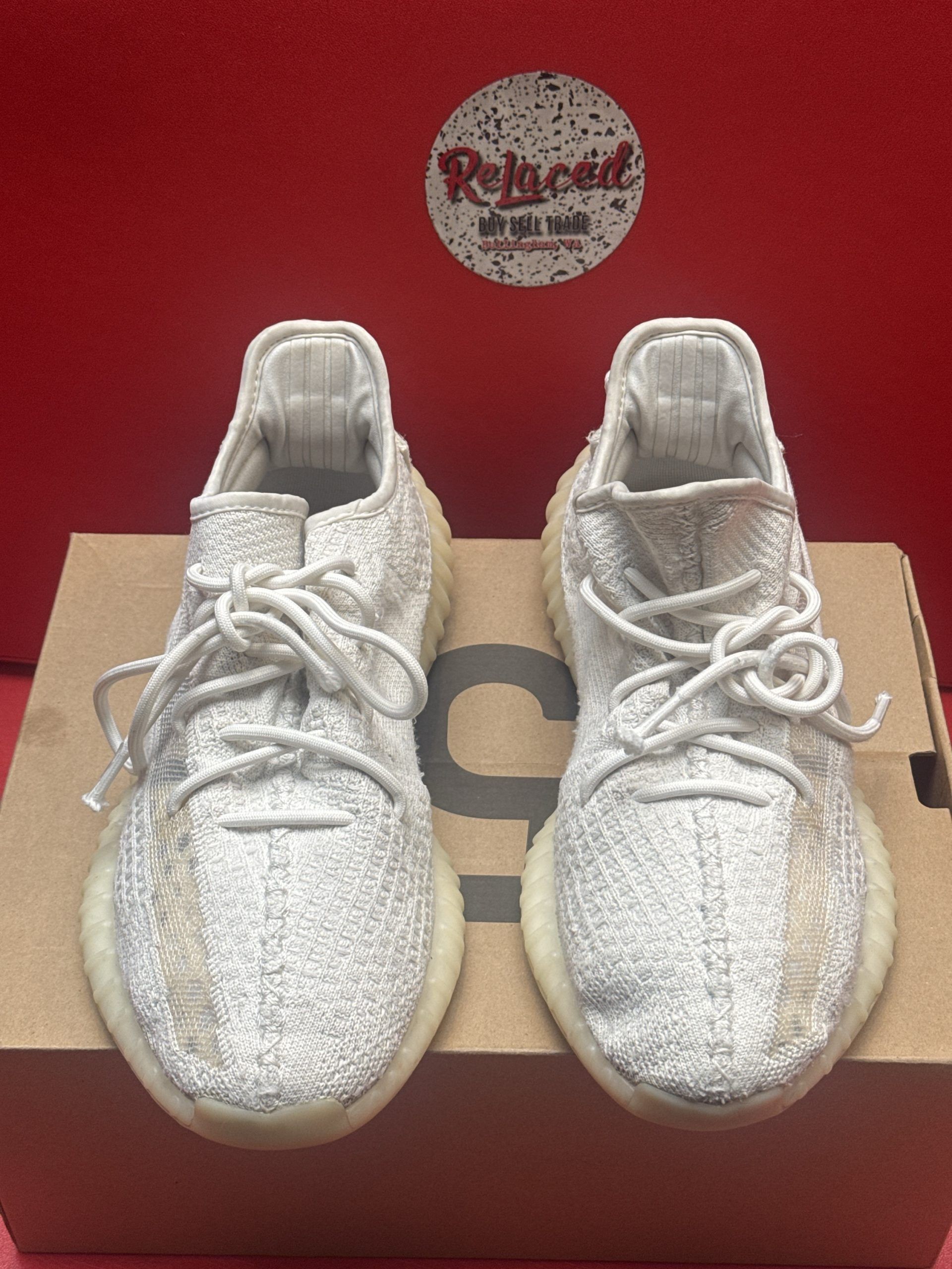 White Yeezy Boost 350 V2 sneakers with a tan sole and shoebox on a red surface.