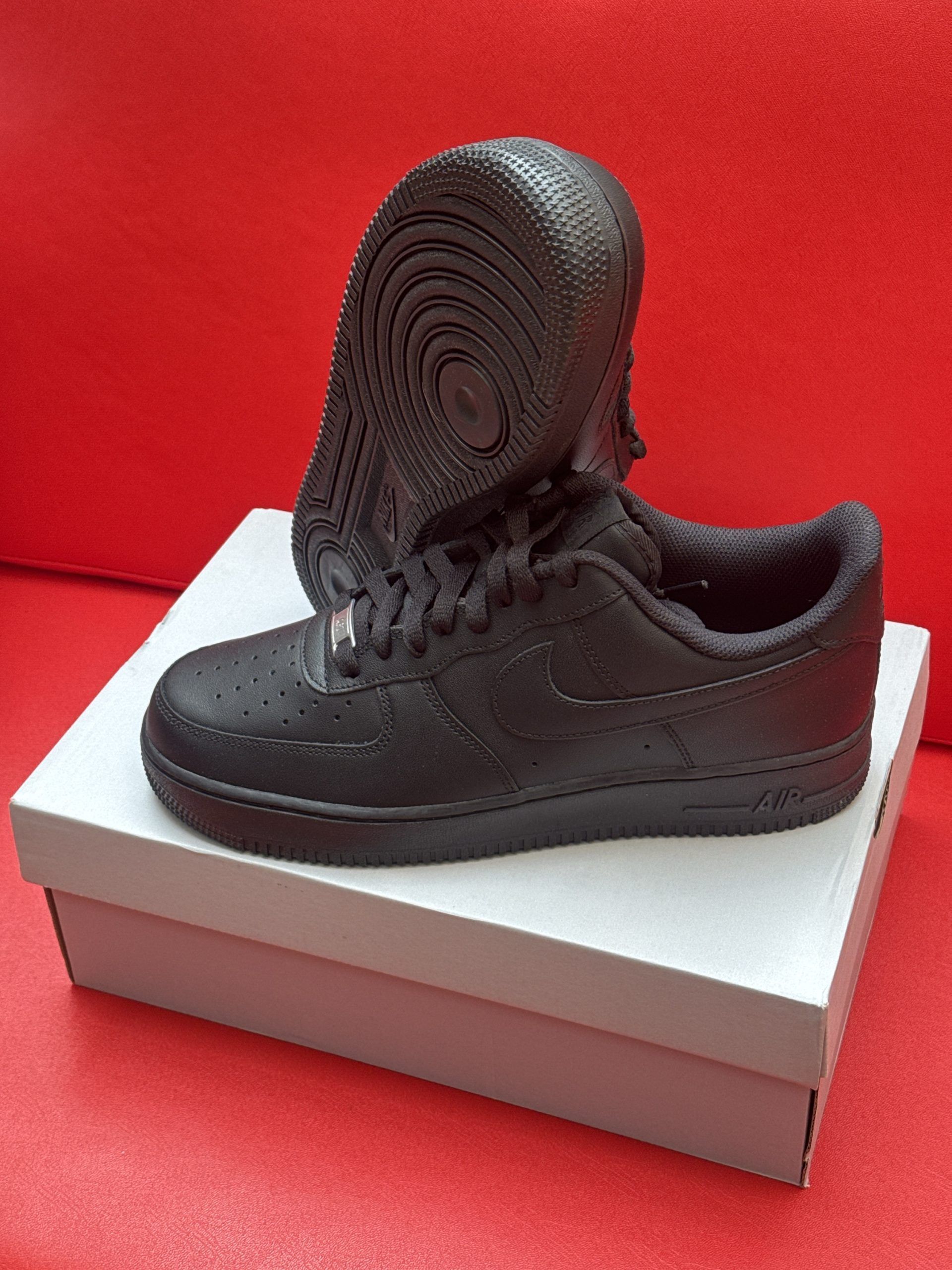 Black Nike Air Force 1 sneakers on a white shoebox against a red background.