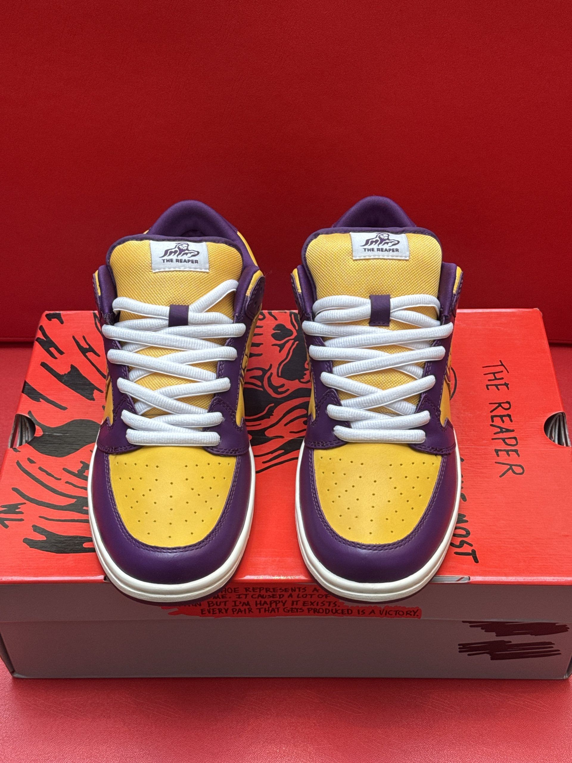 Purple and gold sneakers with a logo on a red patterned shoebox against a red background.