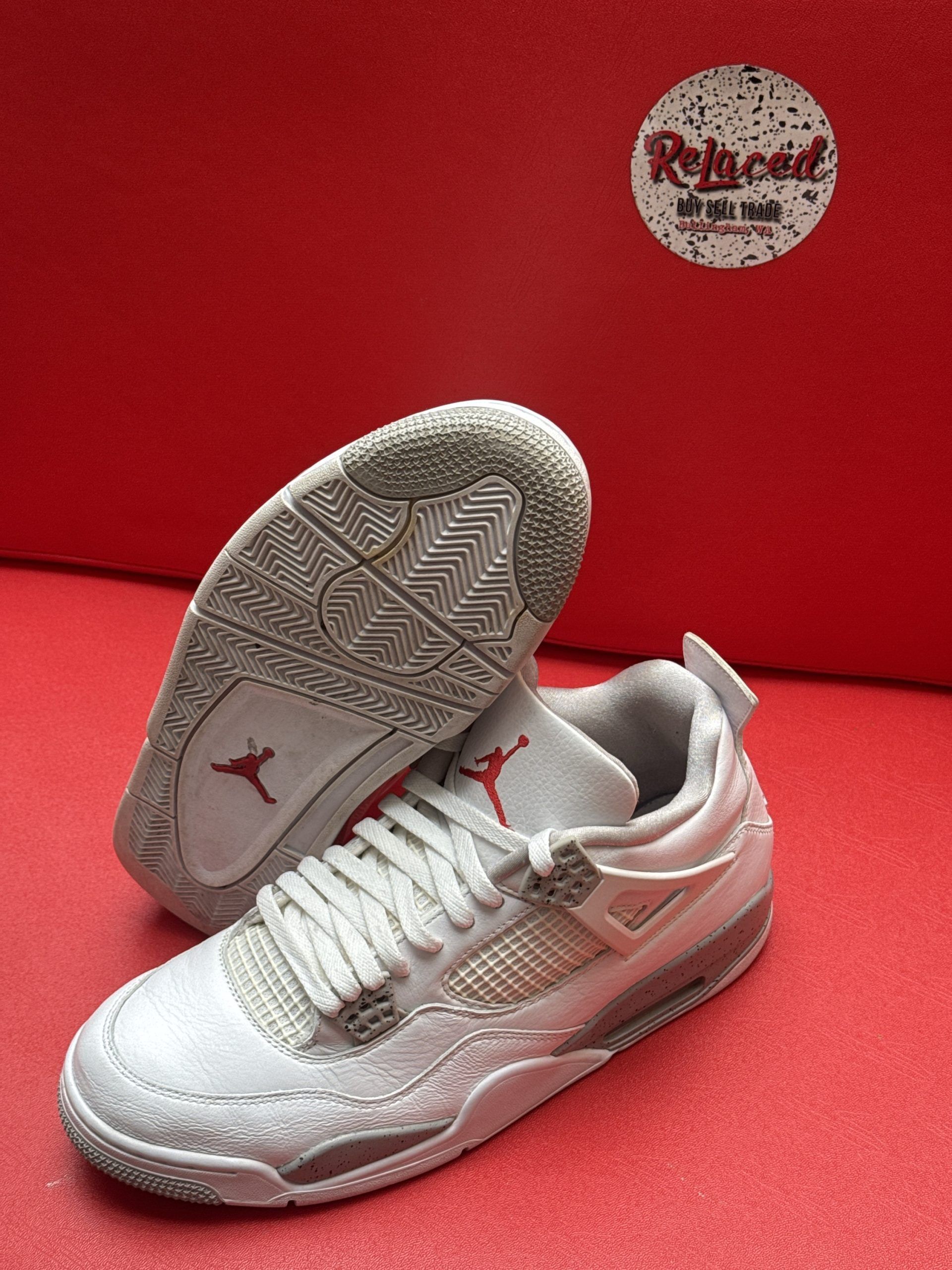 Air Jordan 4 sneakers, white and gray, red logo accents, on red background.