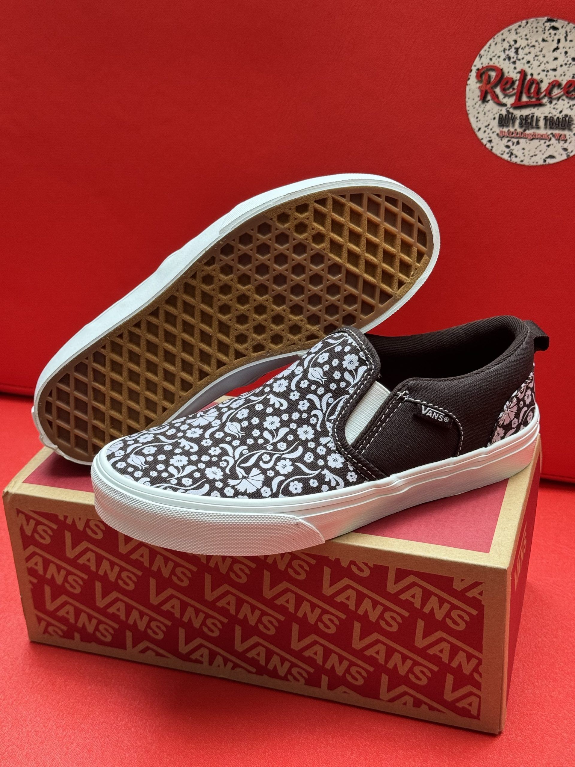 Vans slip-on shoe with a floral pattern and brown accents, resting on a shoebox with the sole visible.