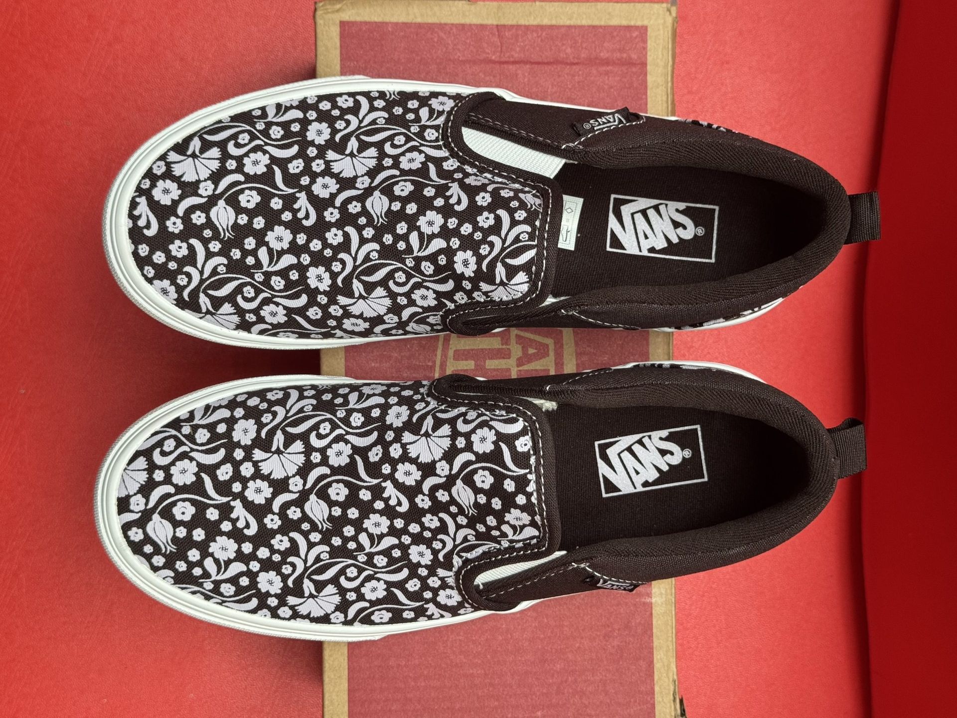 Vans slip-on shoe with a floral pattern and brown accents, resting on a shoebox with the sole visible.