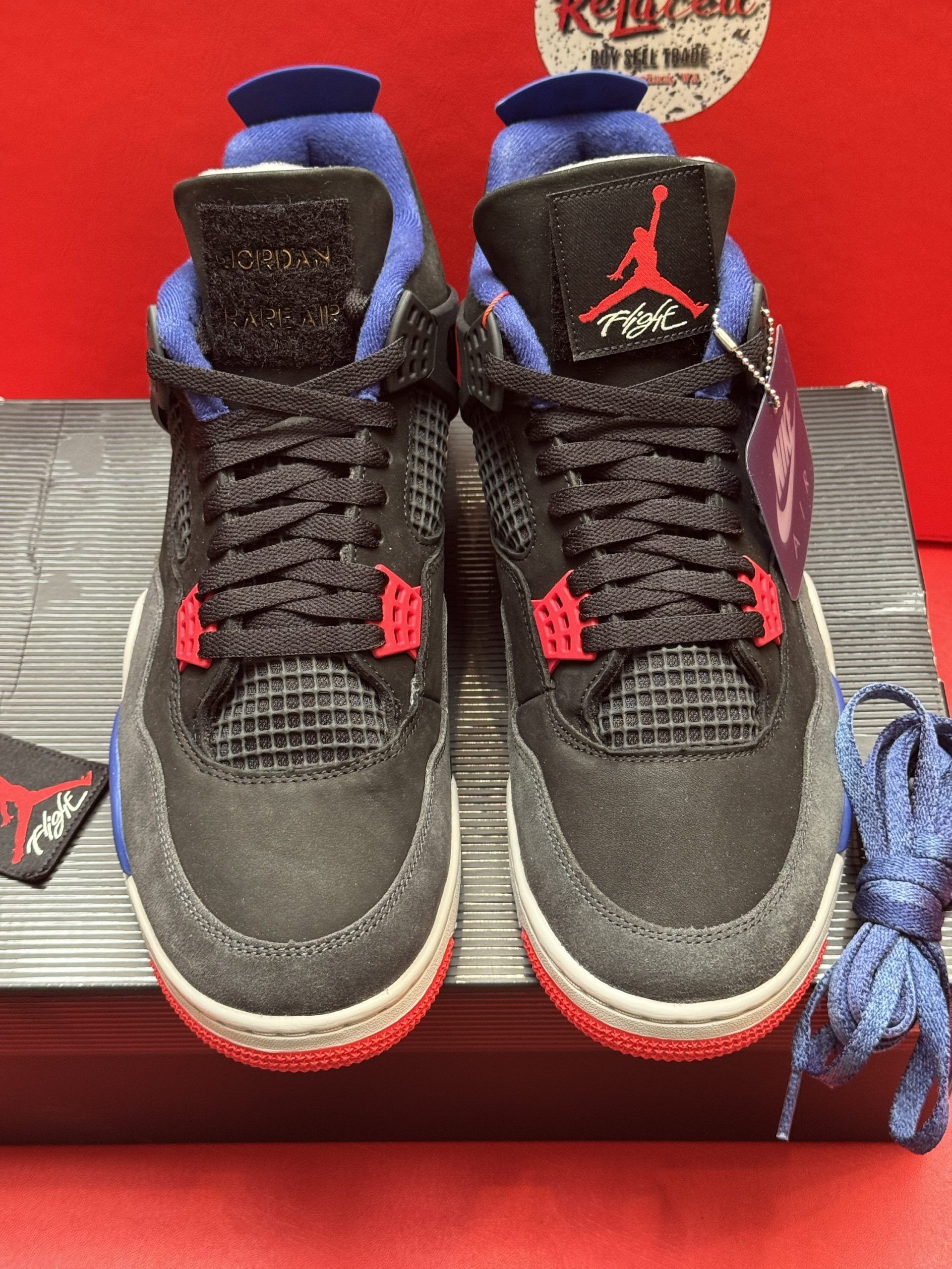 Black, red, and blue Air Jordan 4 sneaker with tag on top of a shoebox.