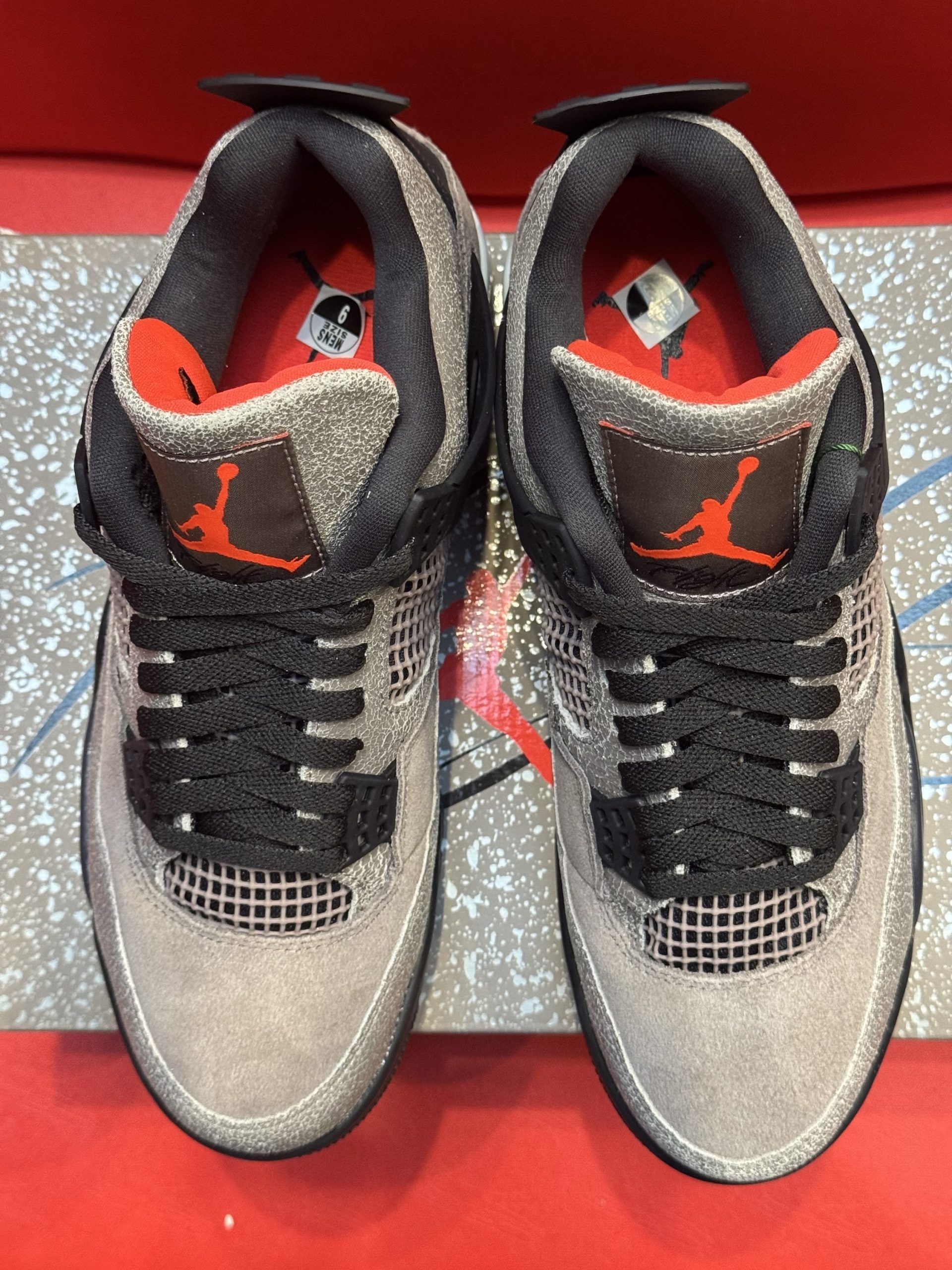 Air Jordan 4 sneakers, gray suede, black accents, sitting on a box, with the sole visible.