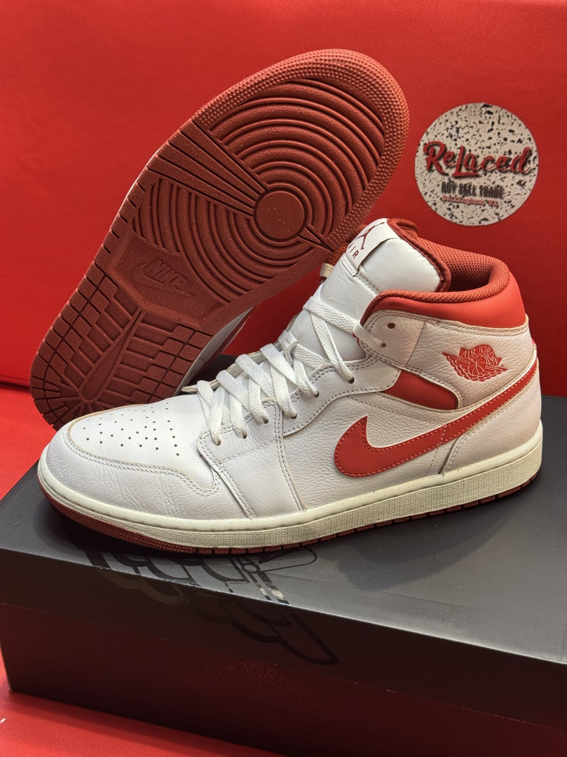 White and red Air Jordan 1 Mid sneaker on black box with red sole visible.