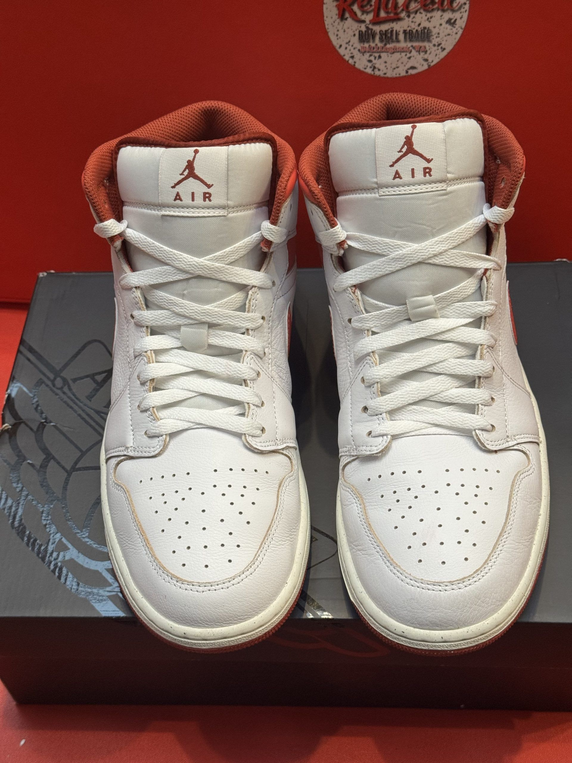 White and red Air Jordan 1 Mid sneaker on black box with red sole visible.