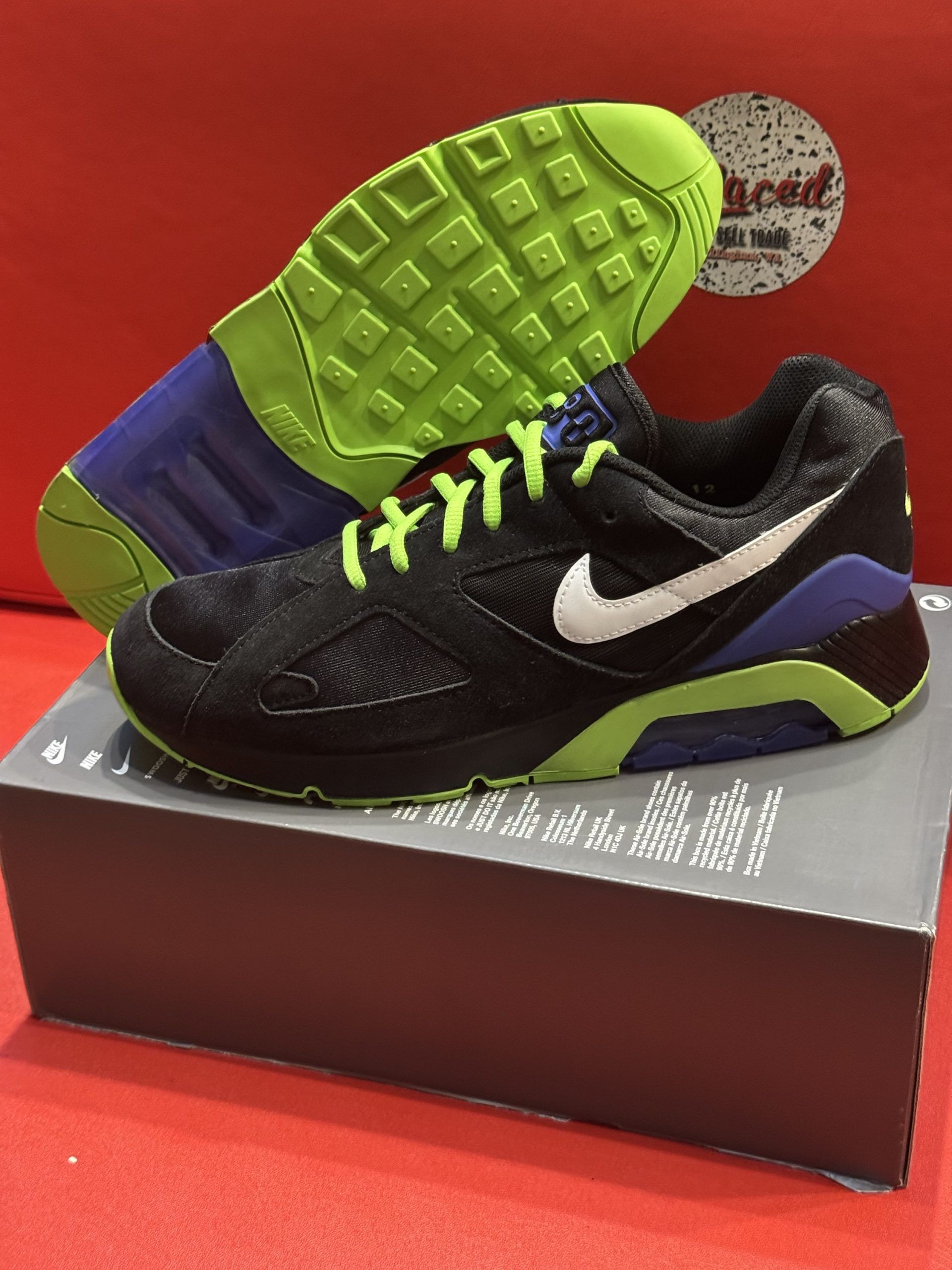 Black Nike Air 180 sneakers with a white swoosh, sitting on a shoebox. Green and blue accents.