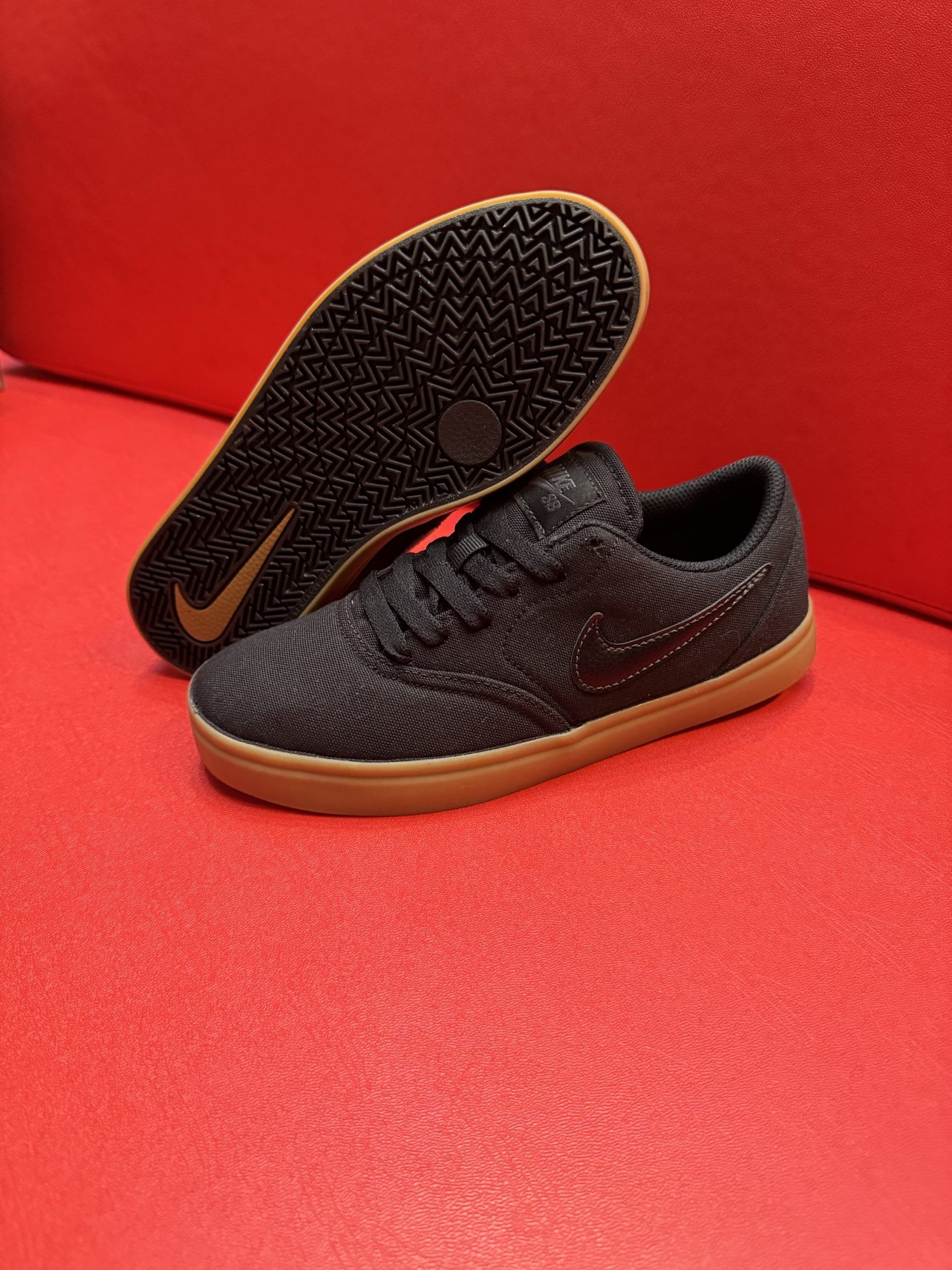 Black Nike sneakers with brown soles on a red surface. One shoe is flipped over to show the sole.