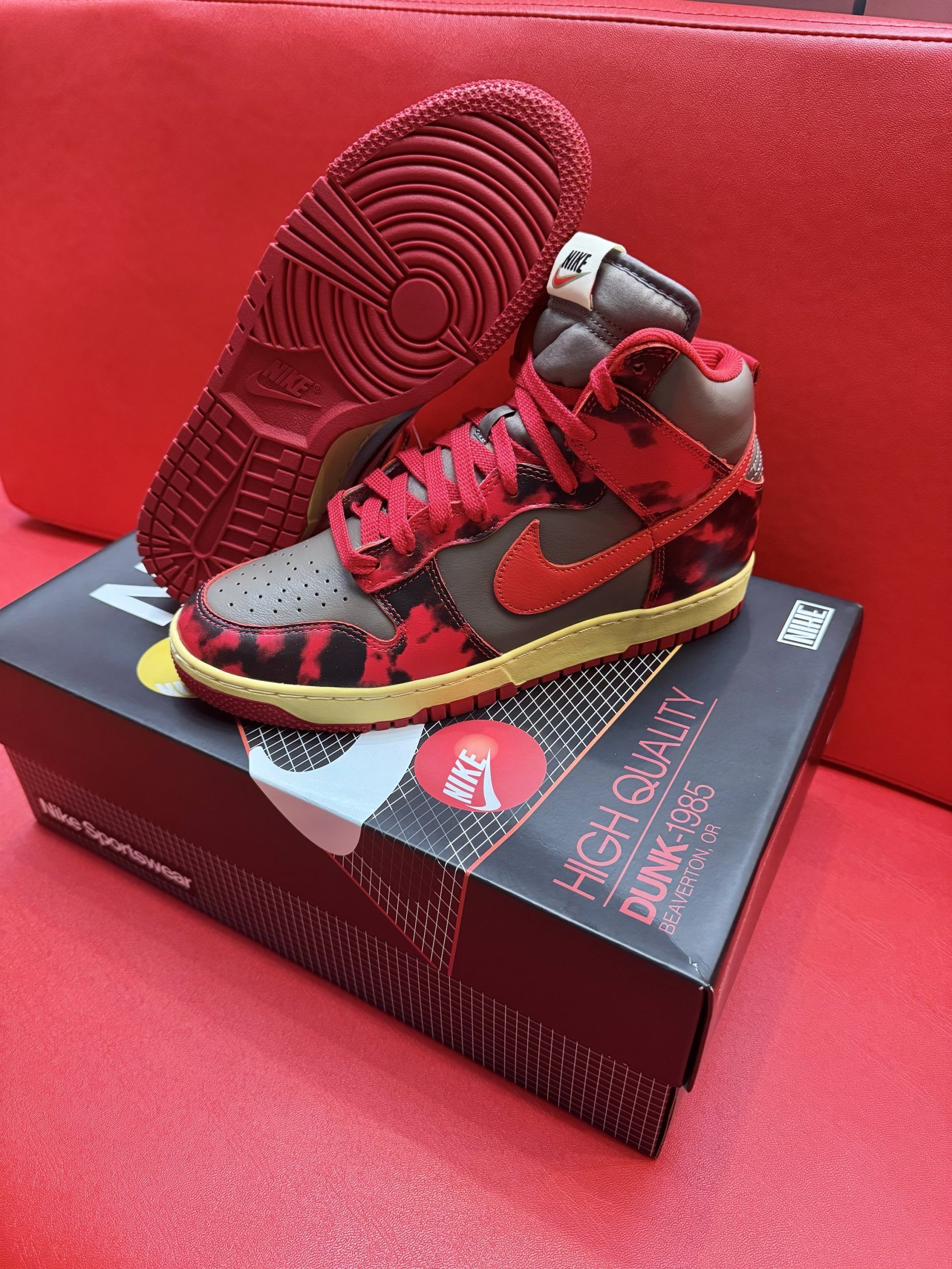 Nike Dunk High sneakers, red and brown camouflage design, on a black box, with a red sole.