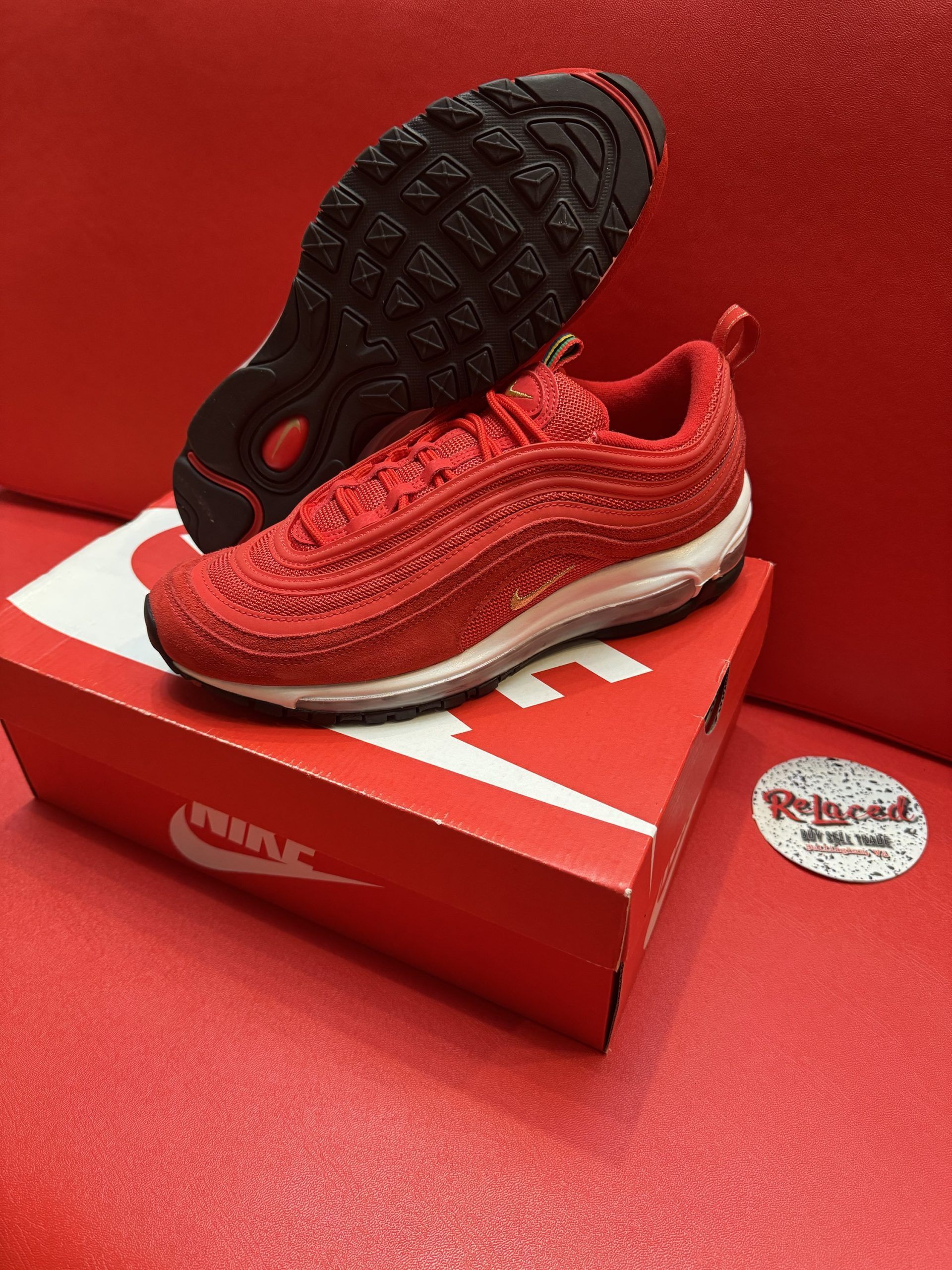 Red Nike Air Max 97 sneakers on a red Nike box, against a red backdrop.