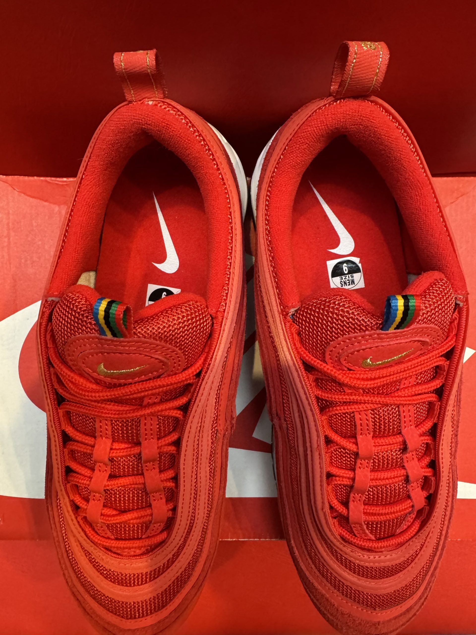Red Nike Air Max 97 sneakers on a red Nike box, against a red backdrop.