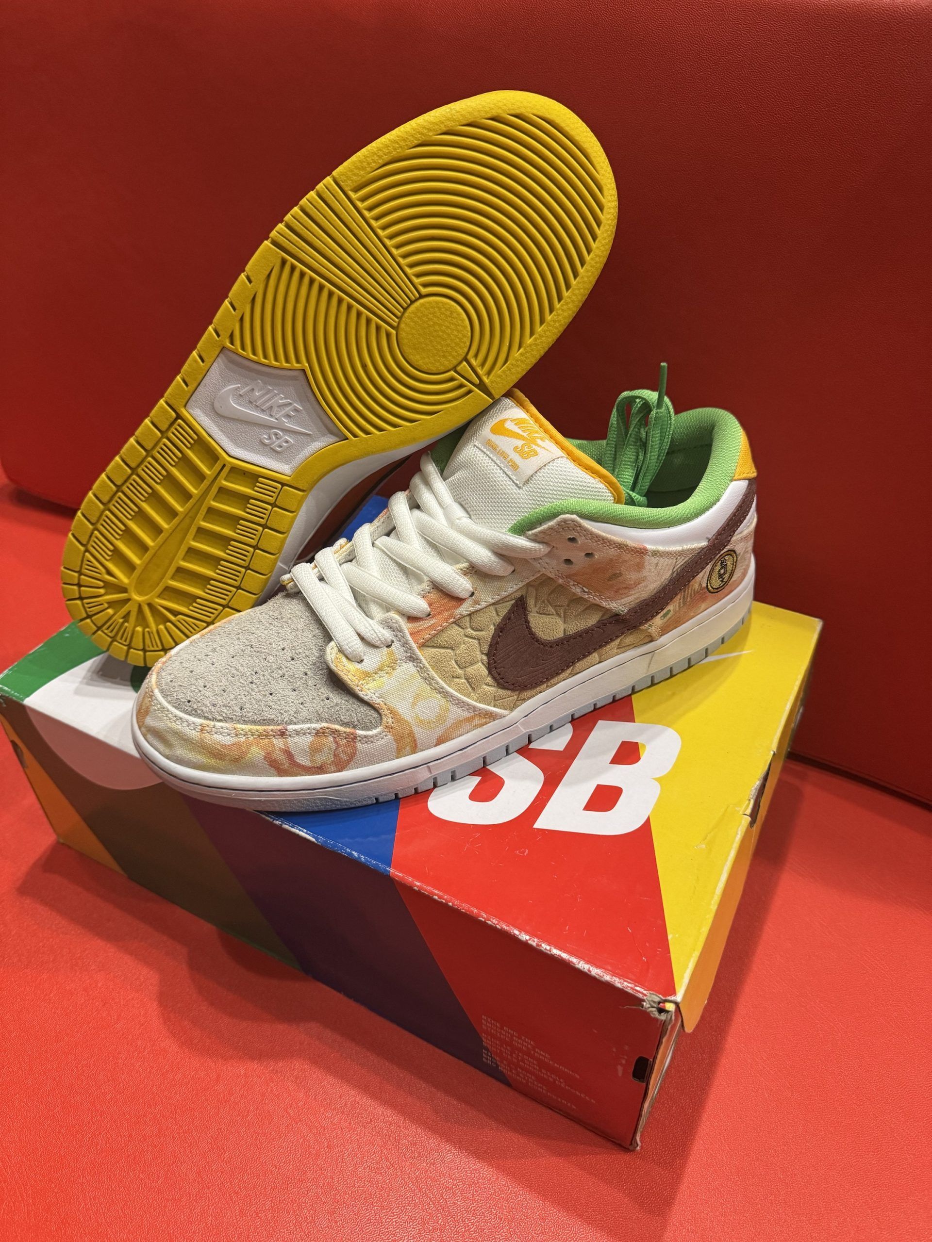 Nike SB Dunk Low sneakers on box, yellow sole, tan, brown and green design.