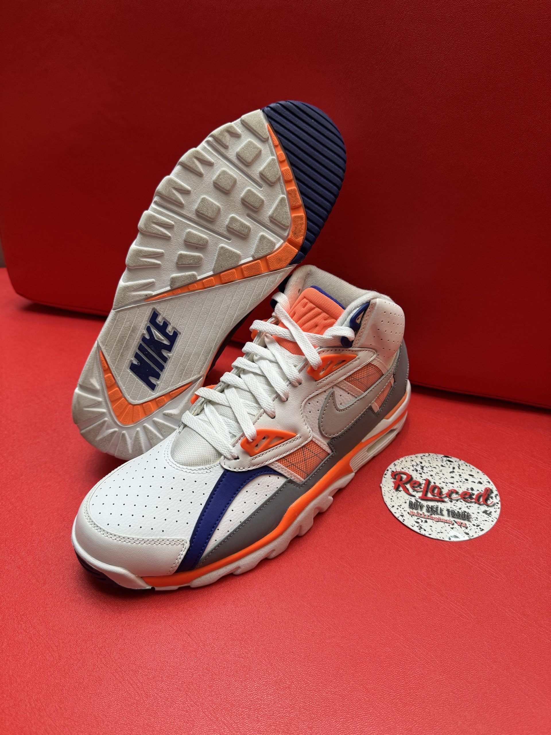 White Nike Air Trainer sneakers with orange and blue accents, on red surface.