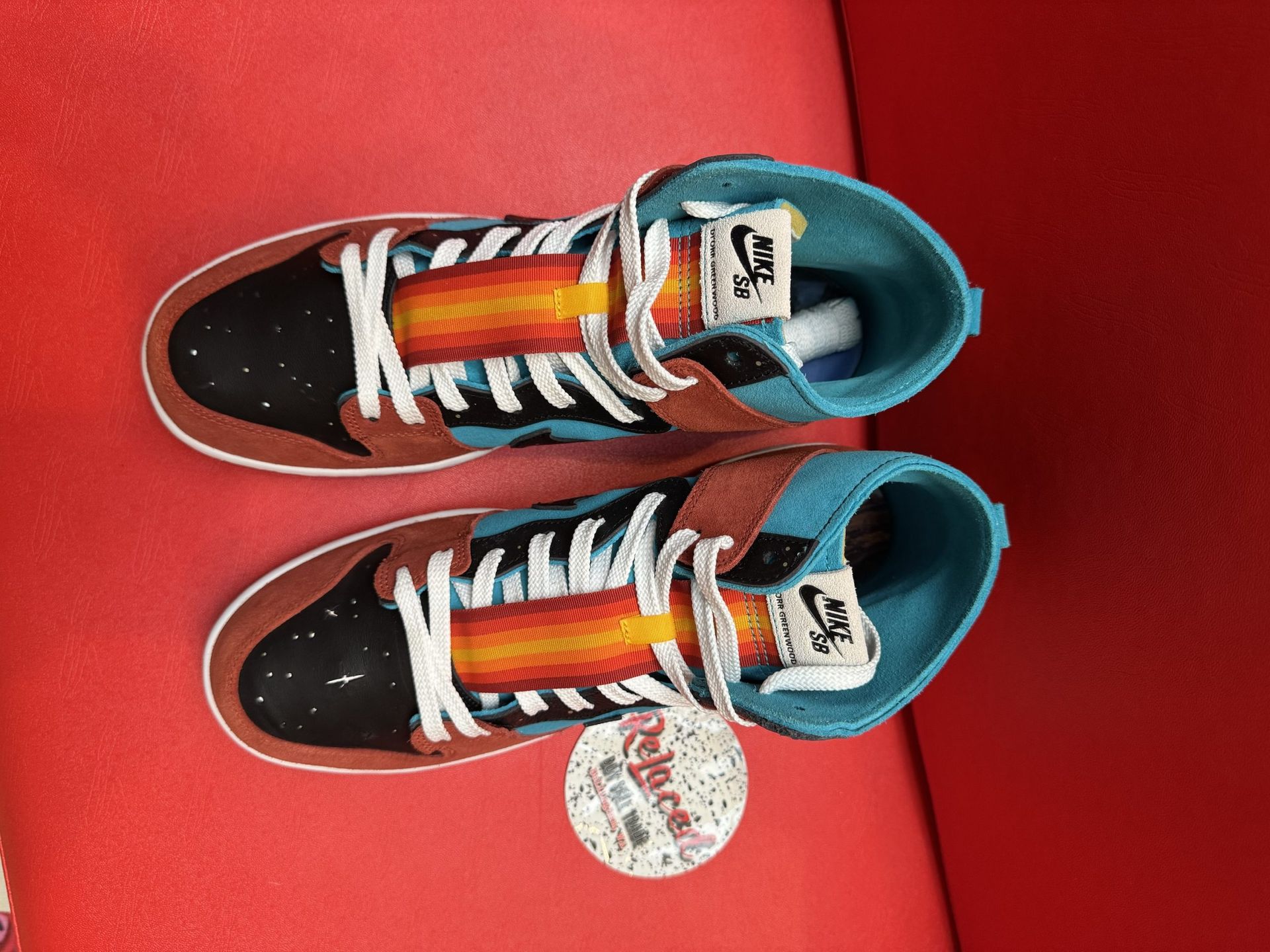 Pair of Nike sneakers, black, teal, and brown, with a white sole, on a red surface.