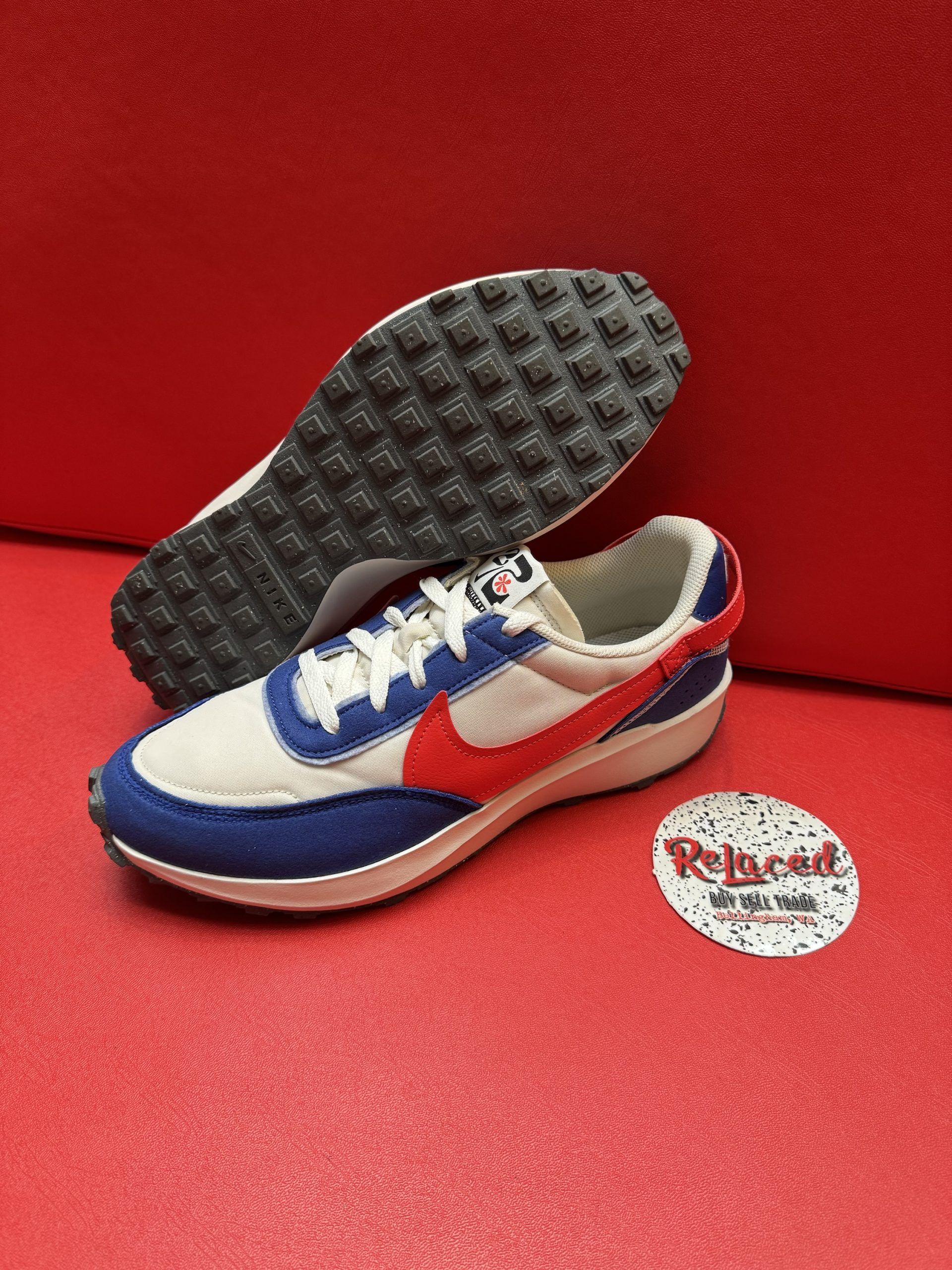 Blue, red, and white Nike running shoe on a red surface, with a black waffle sole and a logo sticker.