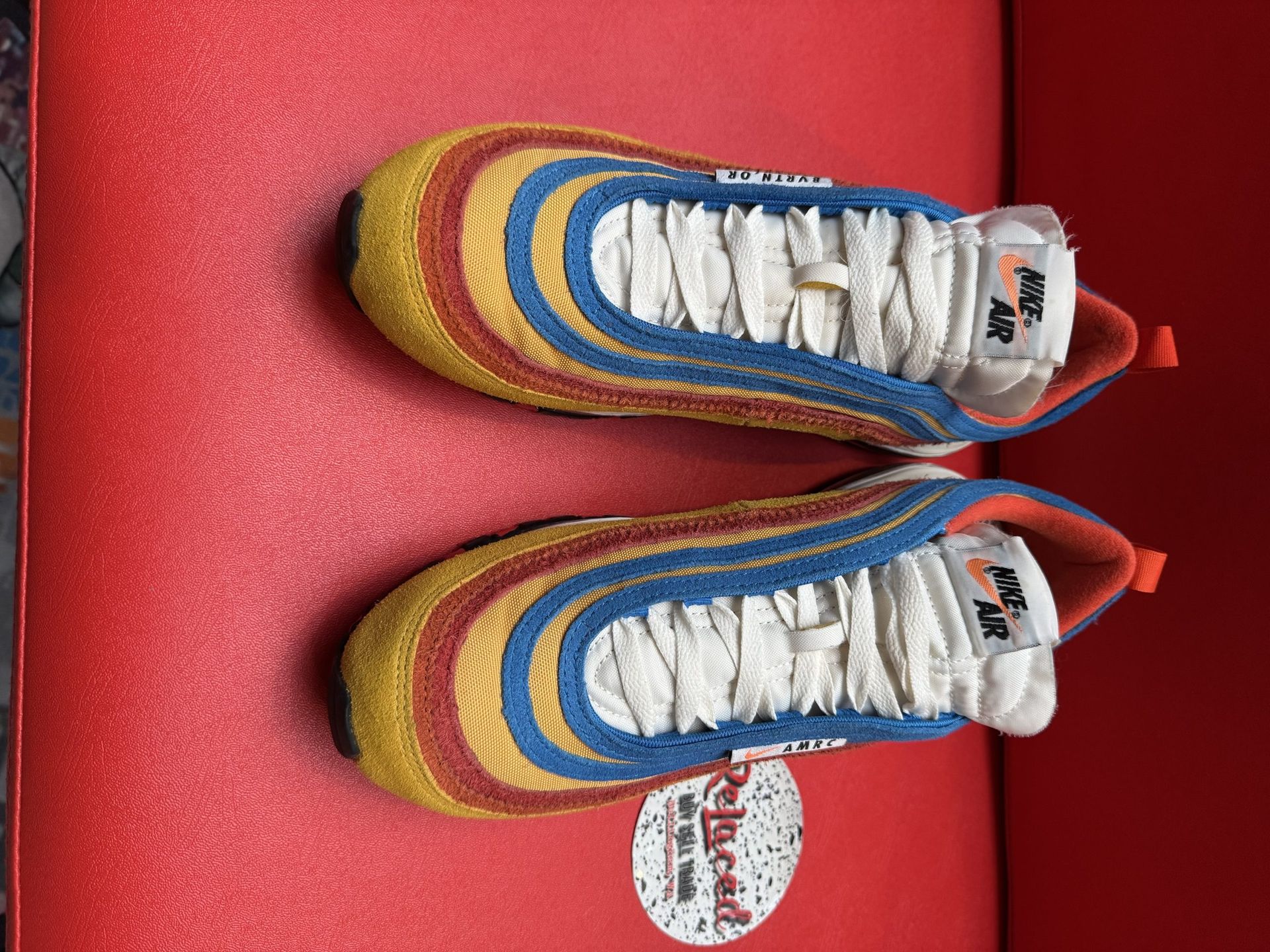 Colorful Nike Air Max 97 sneaker with visible sole, resting on a red surface.