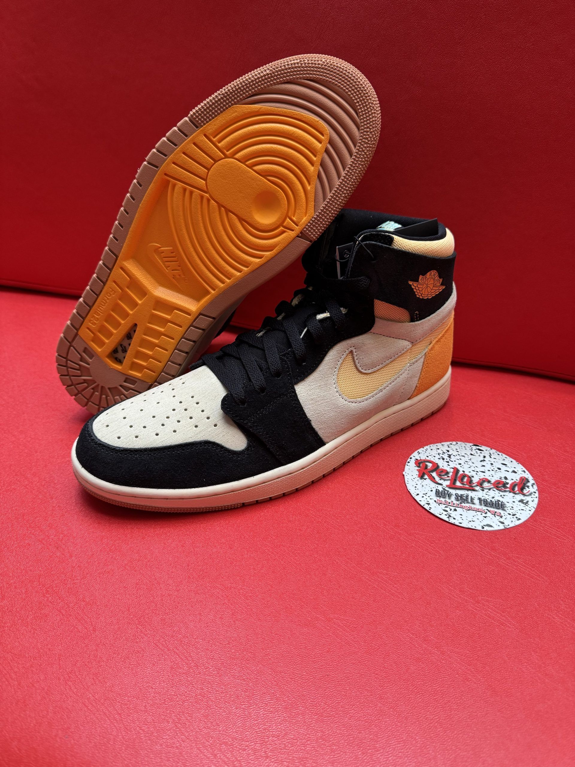 High-top sneaker in black, tan, and gold with a textured sole, resting on a red surface.