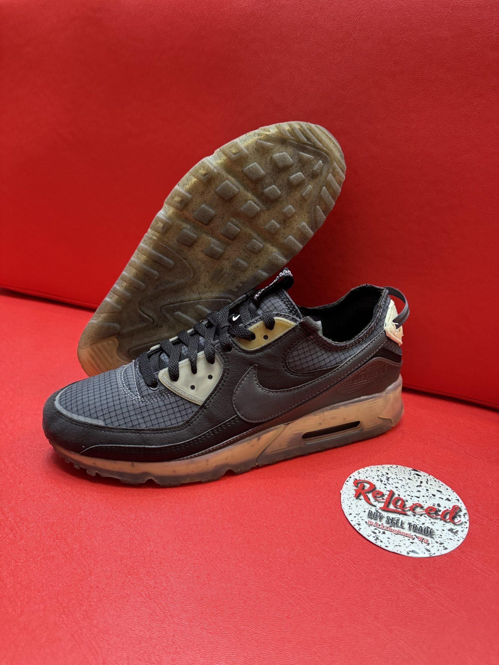 Black Nike Air Max 90 sneaker with tan sole and beige accents, set against a red background.