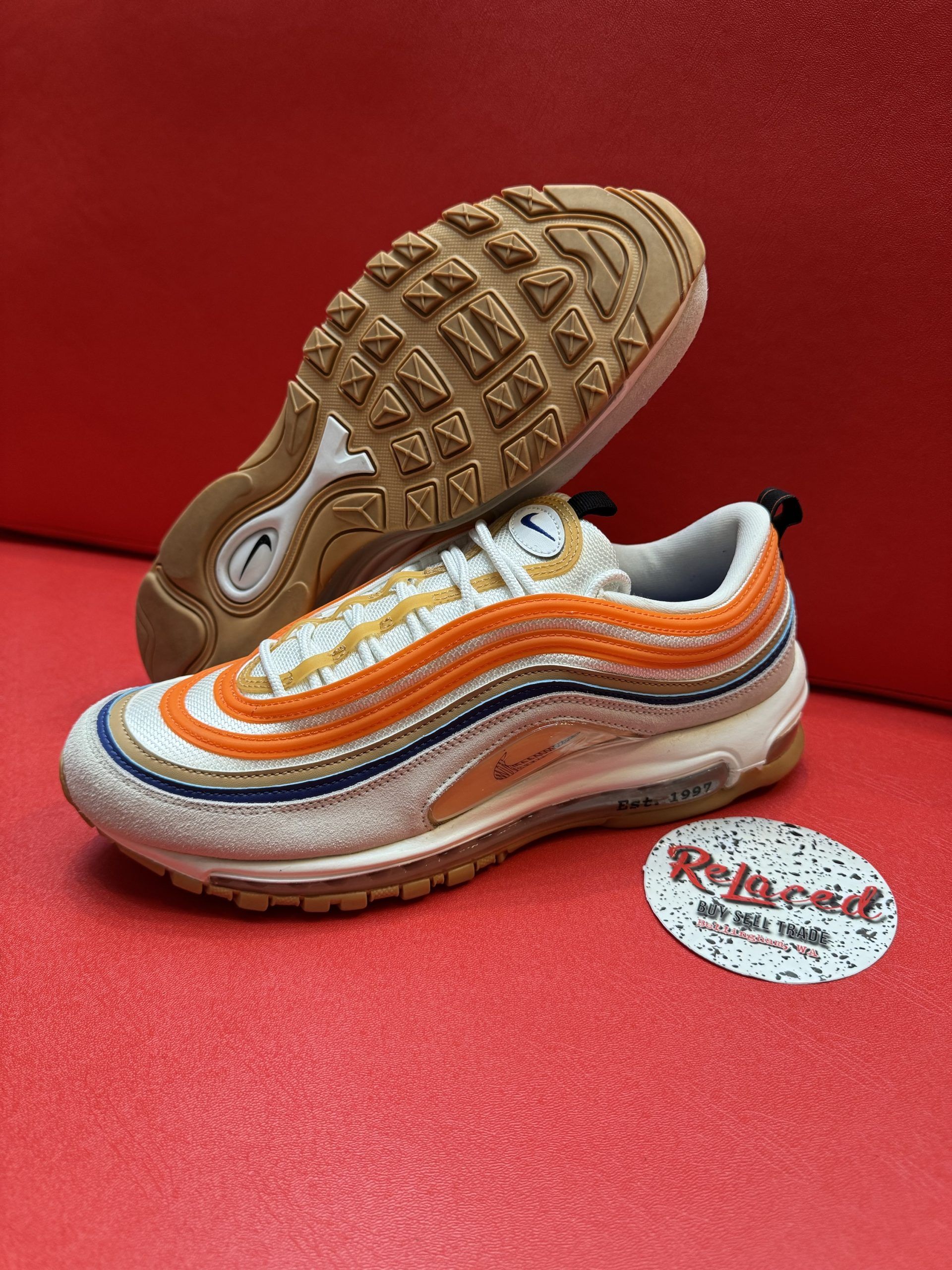 Nike Air Max 97 sneakers with orange and blue stripes on a red surface.