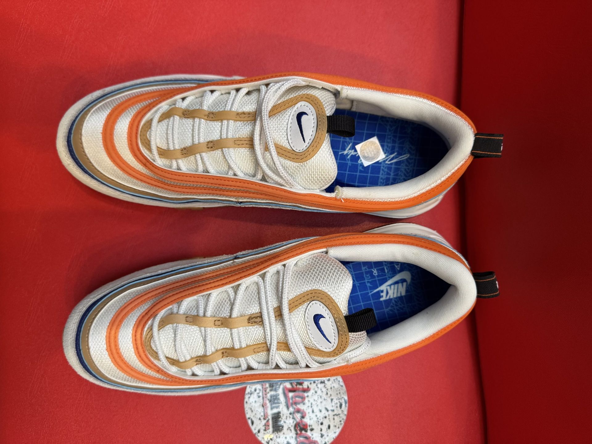 Nike Air Max 97 sneakers with orange and blue stripes on a red surface.