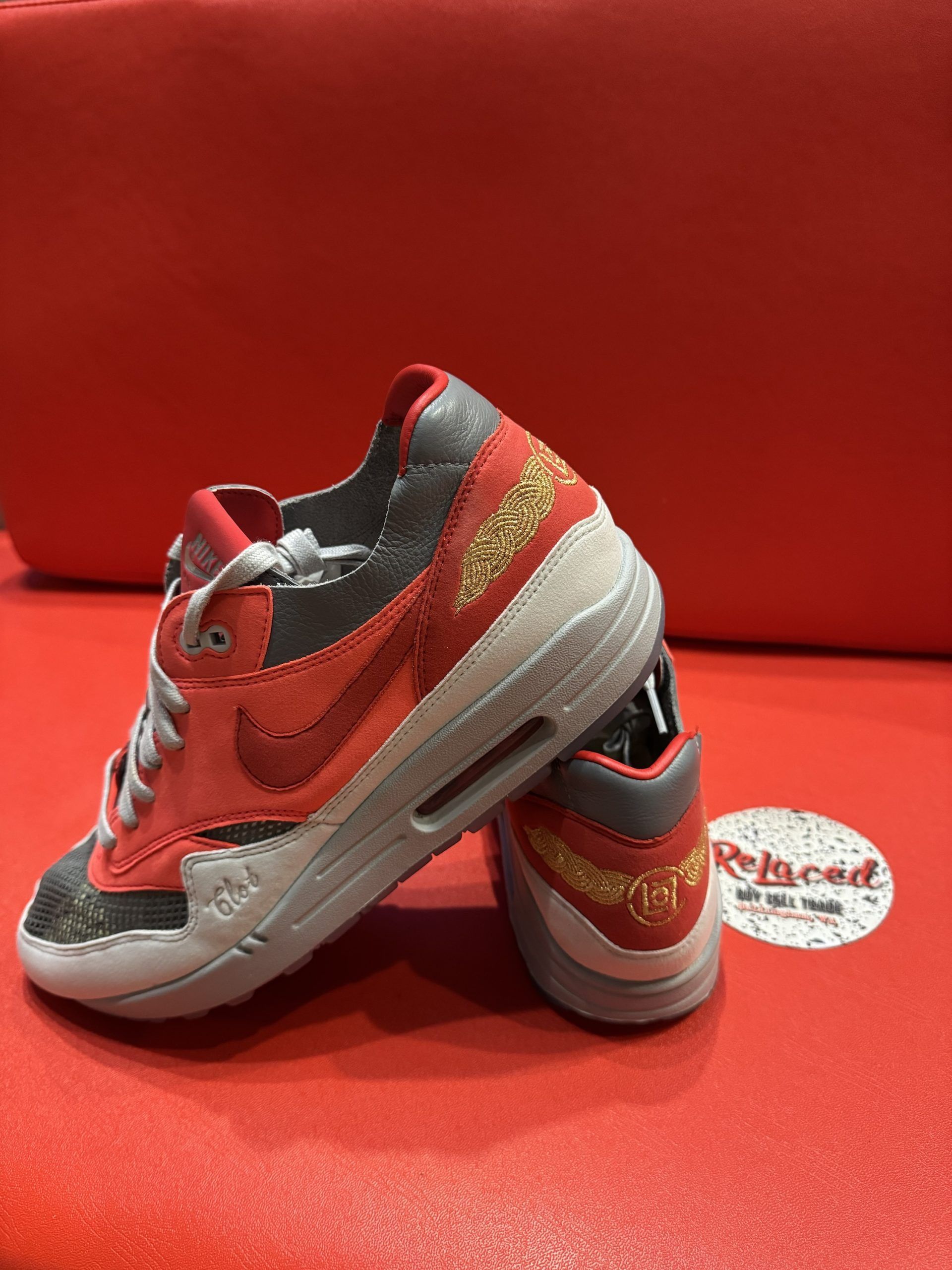 Red and grey Nike Air Max 1 sneaker with a transparent sole, sitting on a red surface.