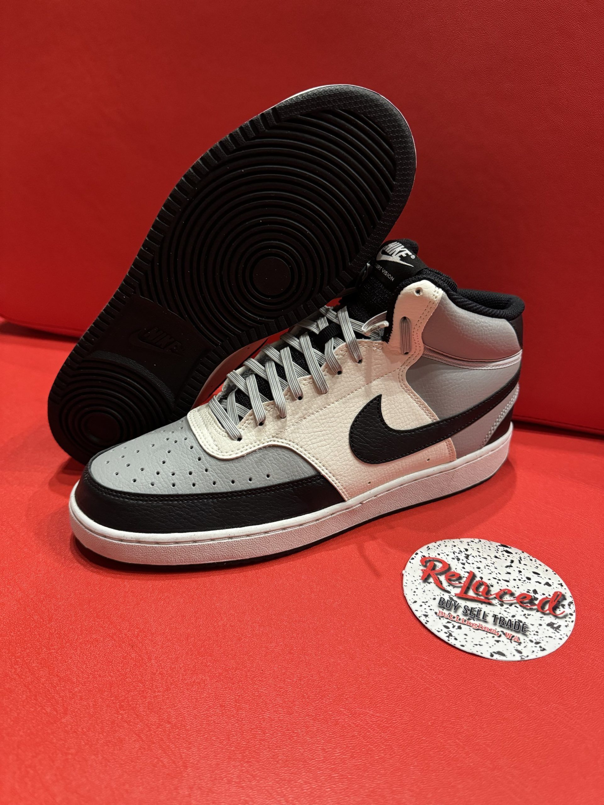 Nike Vandal high-top sneaker with black sole, gray and light tan panels, black swoosh, and a red background.