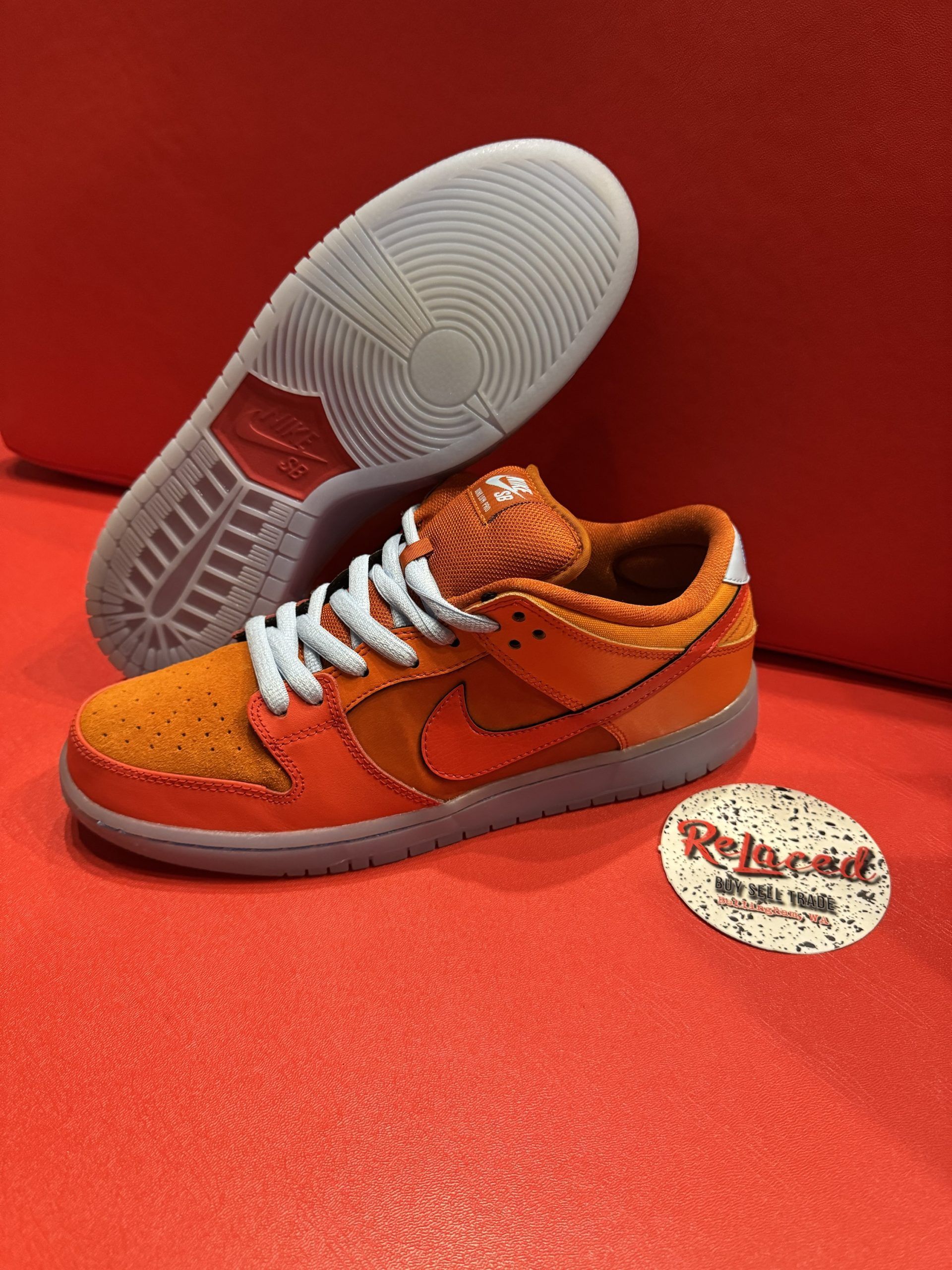 Orange Nike Dunk Low sneakers with blue laces, set on a red surface with the sole visible.