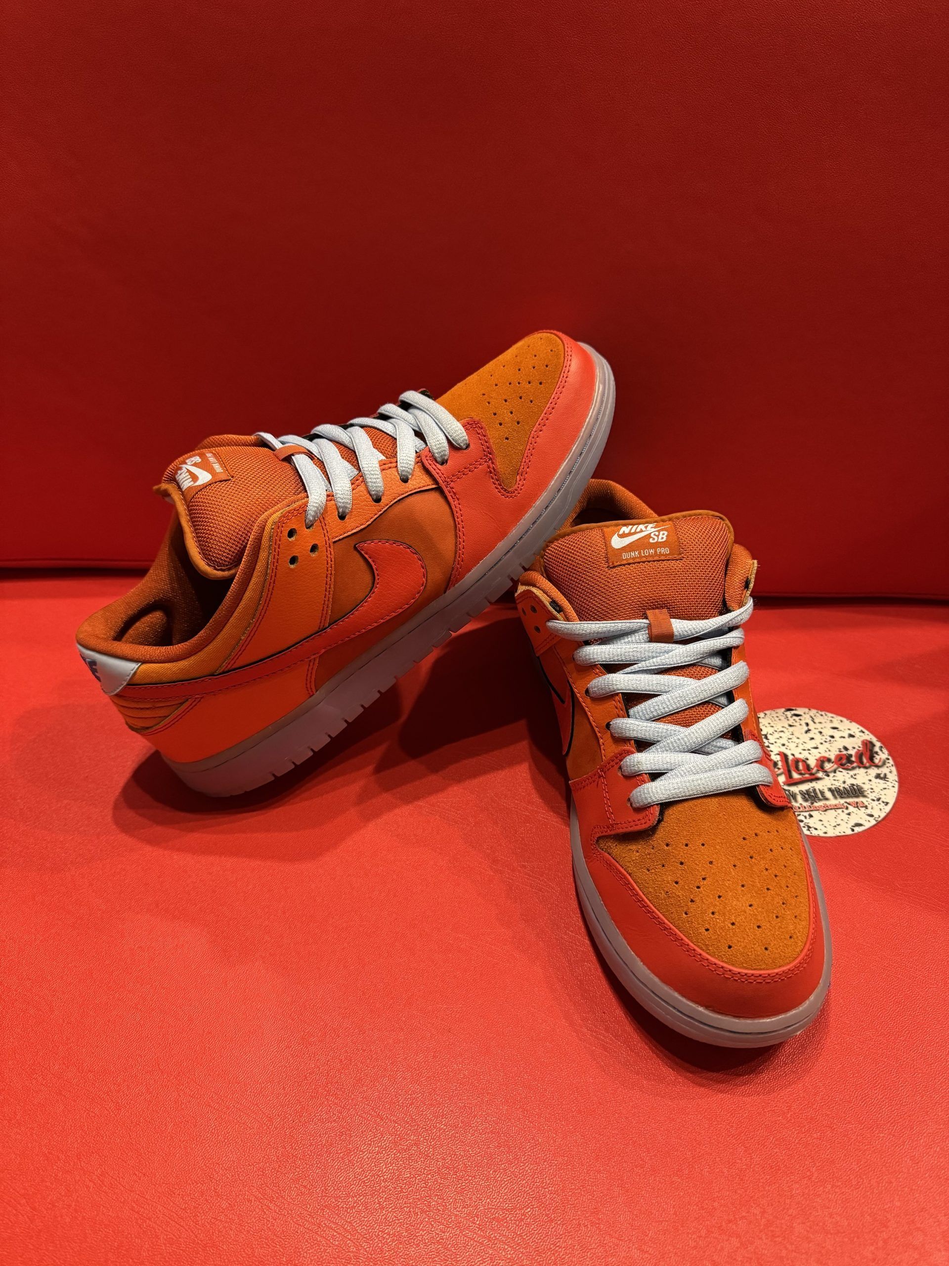 Orange Nike Dunk Low sneakers with blue laces, set on a red surface with the sole visible.