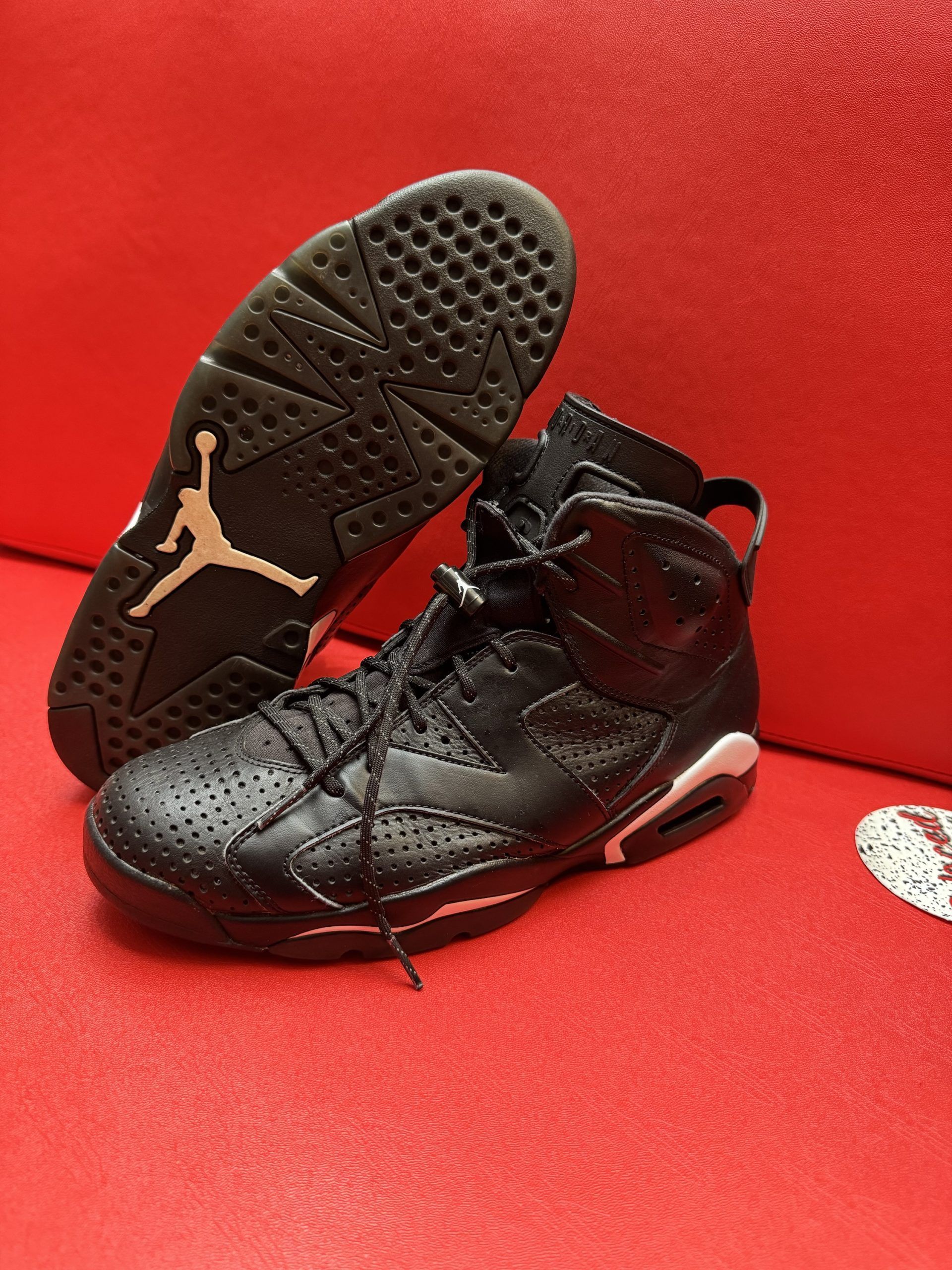 Black Air Jordan 6 sneakers on a red surface, showcasing the sole with a Jumpman logo.