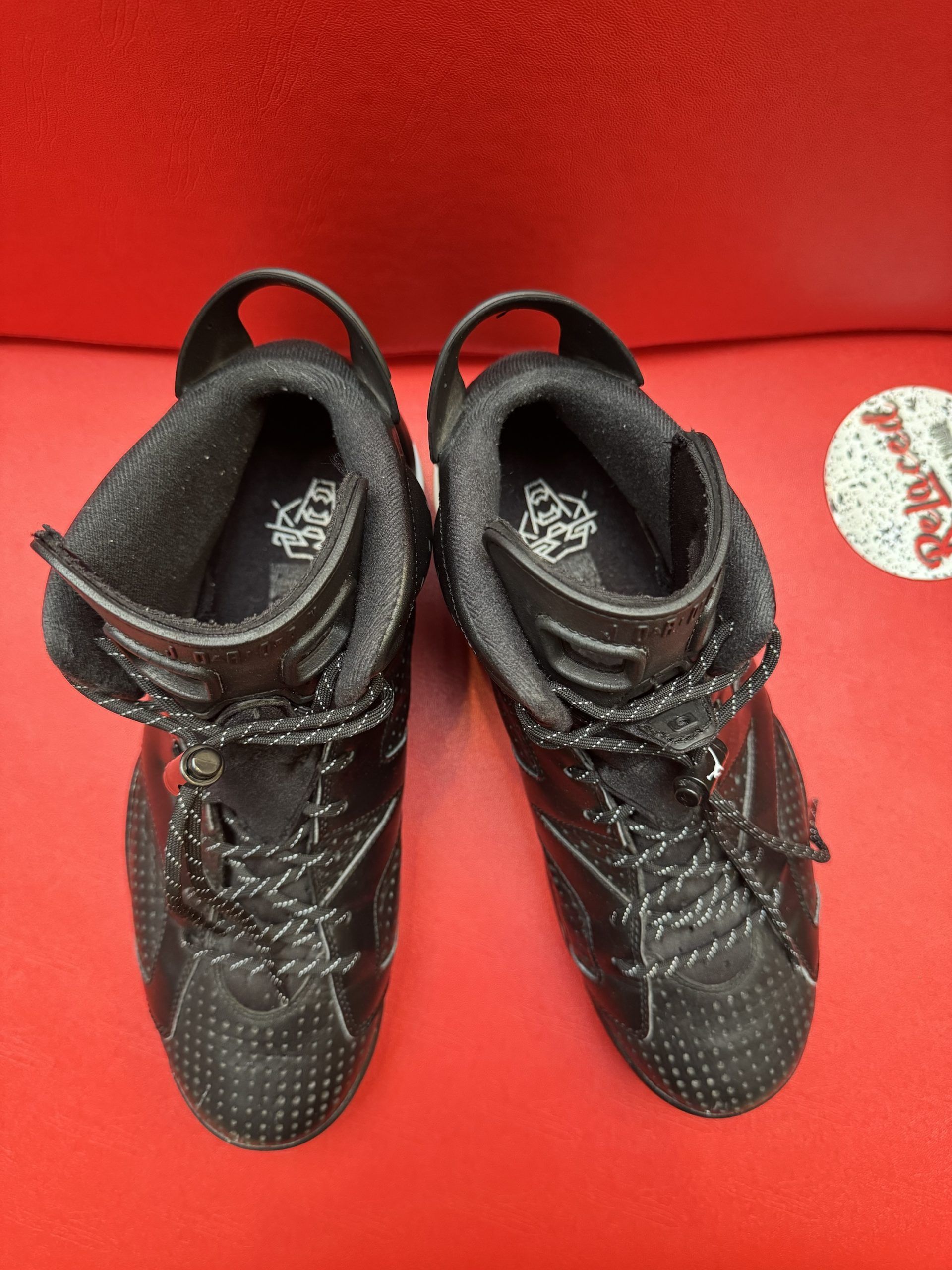 Black Air Jordan 6 sneakers on a red surface, showcasing the sole with a Jumpman logo.