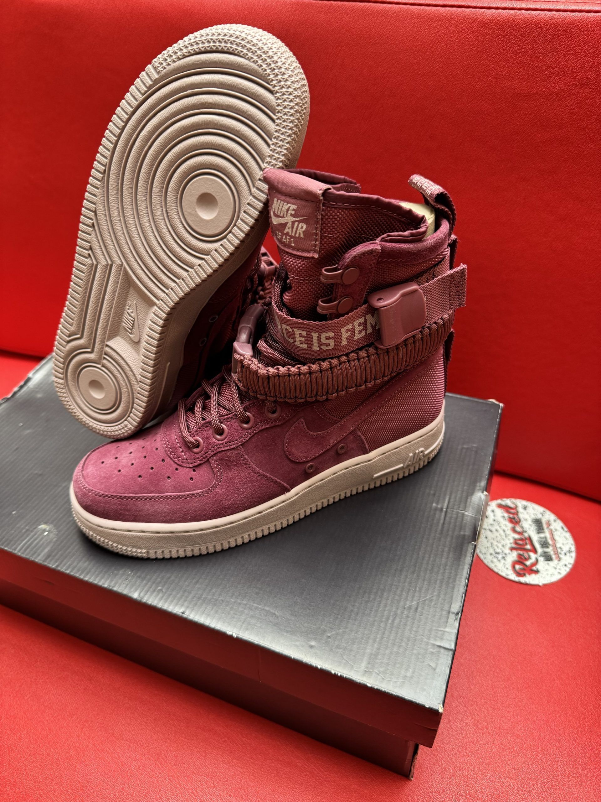 Burgundy Nike Air Force 1 high-top sneakers on a box, with one sole facing upward on a red surface.