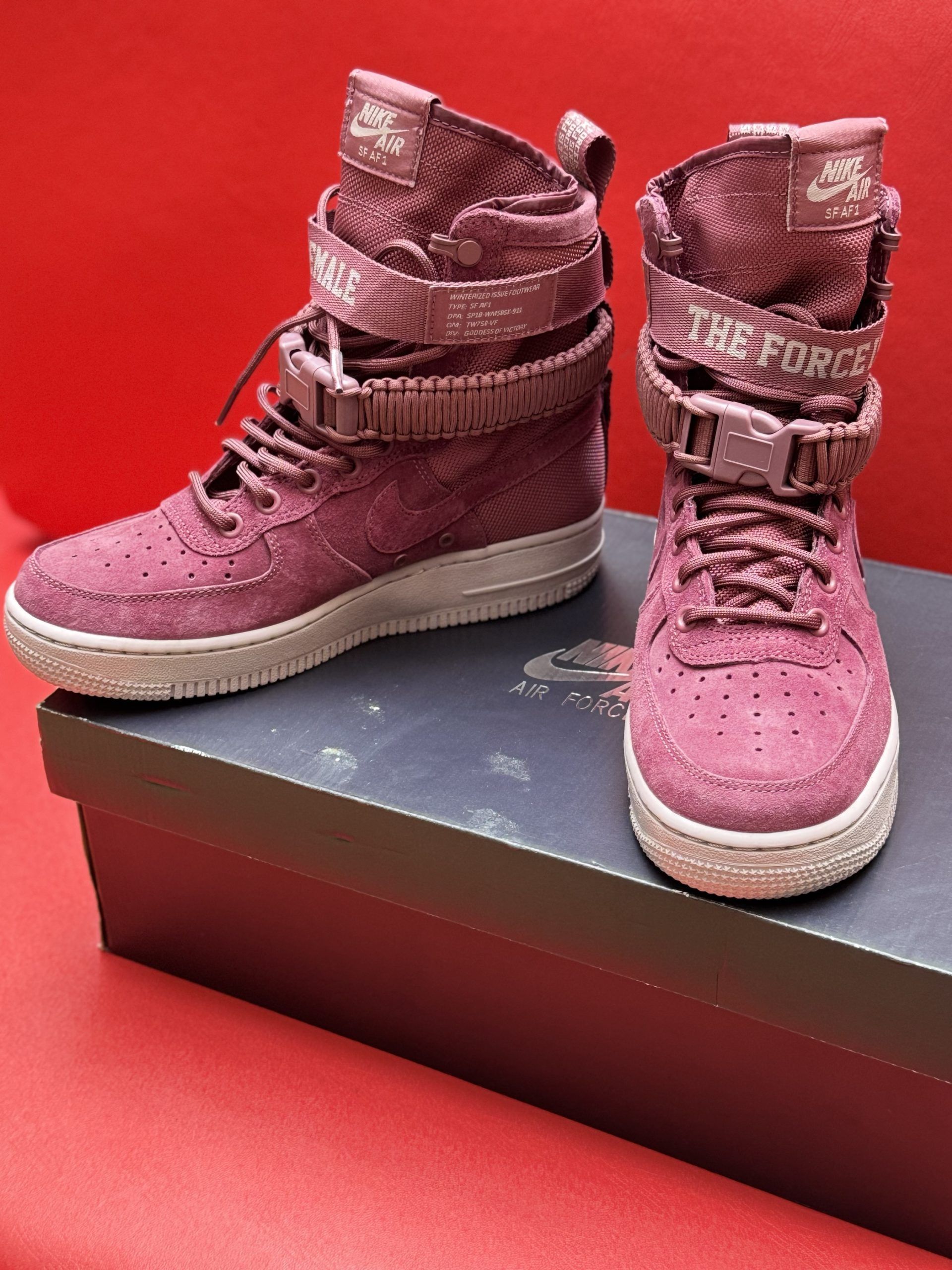 Burgundy Nike Air Force 1 high-top sneakers on a box, with one sole facing upward on a red surface.