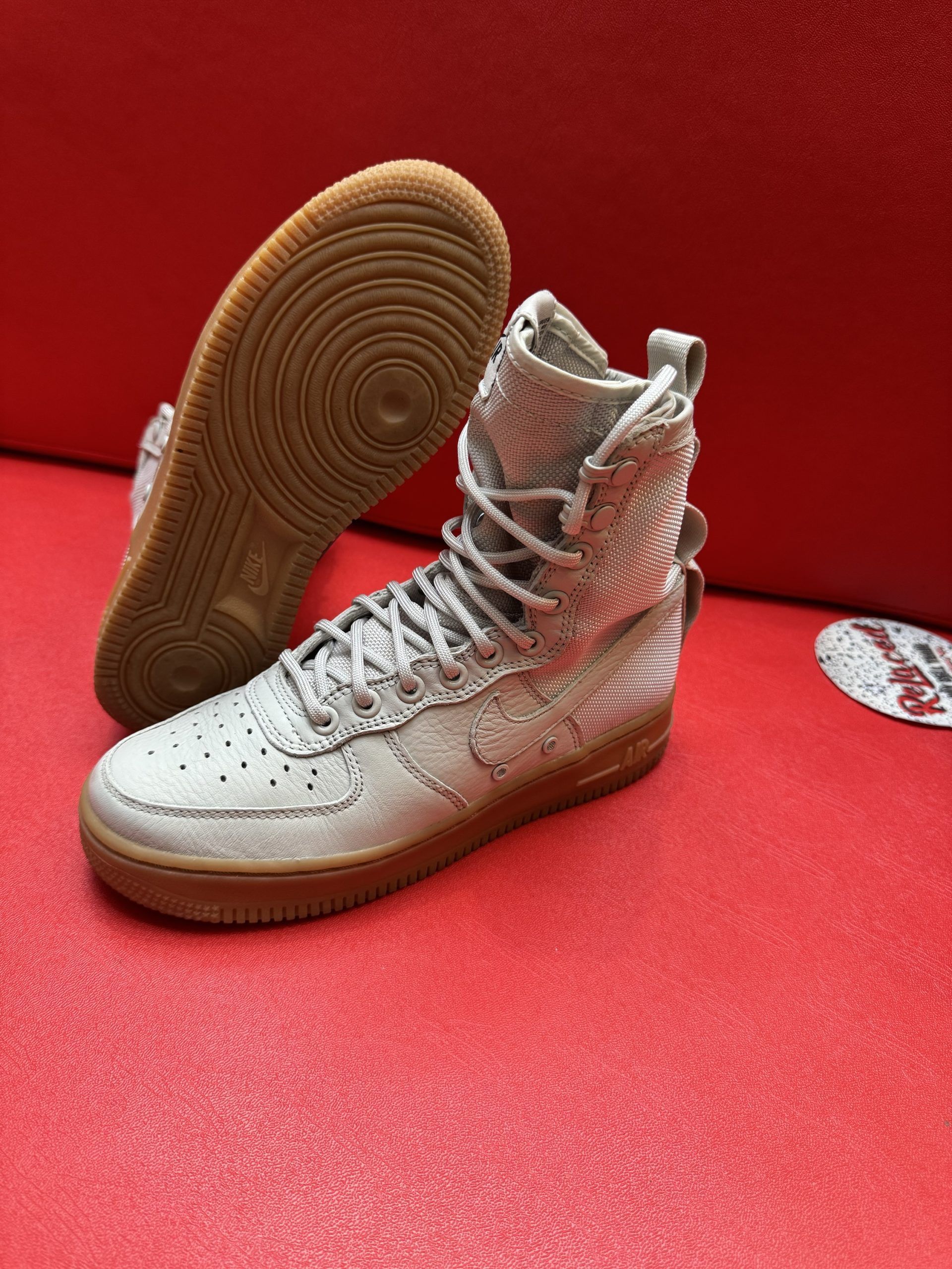 High-top Nike Air Force 1 sneakers in tan and cream colors with brown soles, on a red surface.