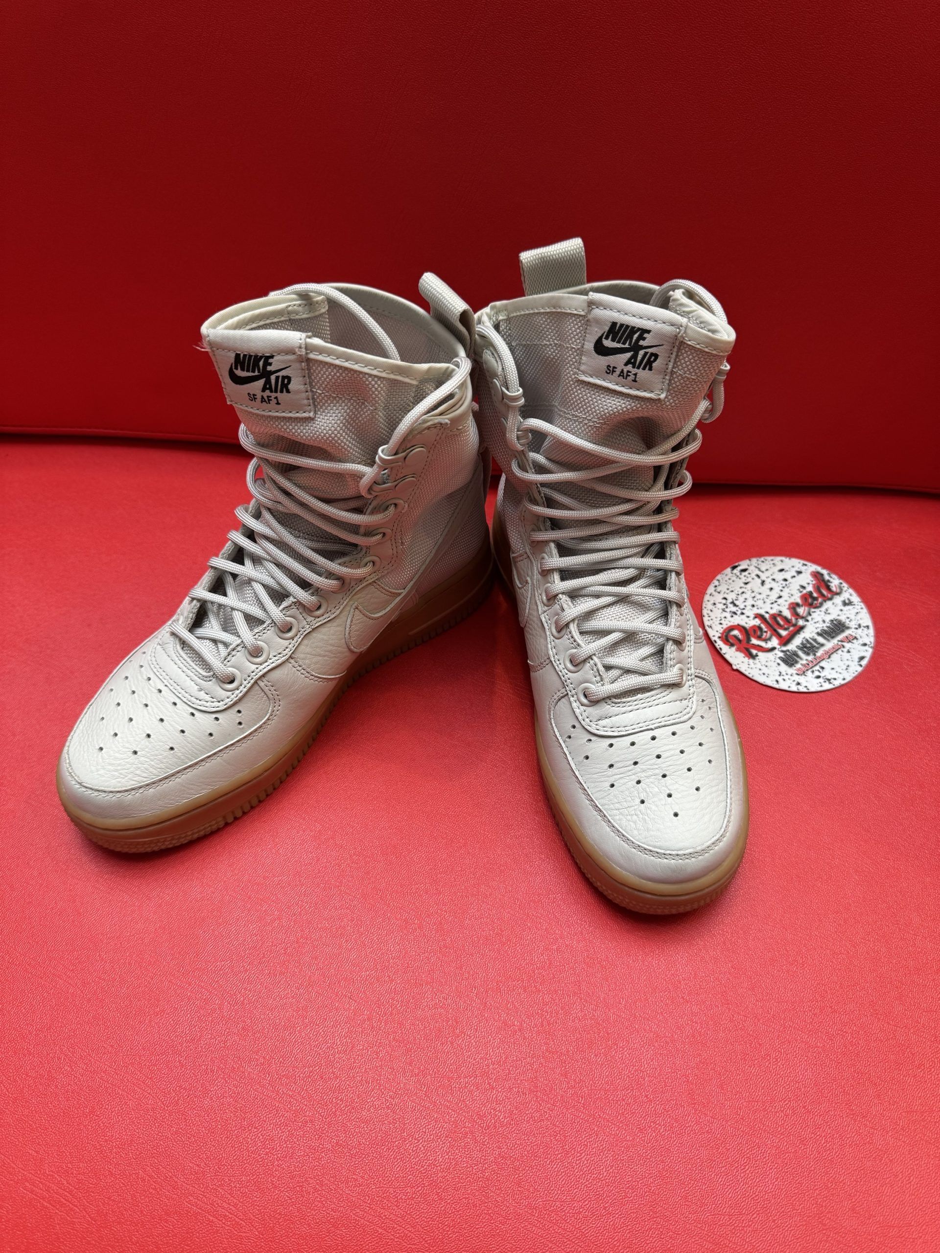 High-top Nike Air Force 1 sneakers in tan and cream colors with brown soles, on a red surface.