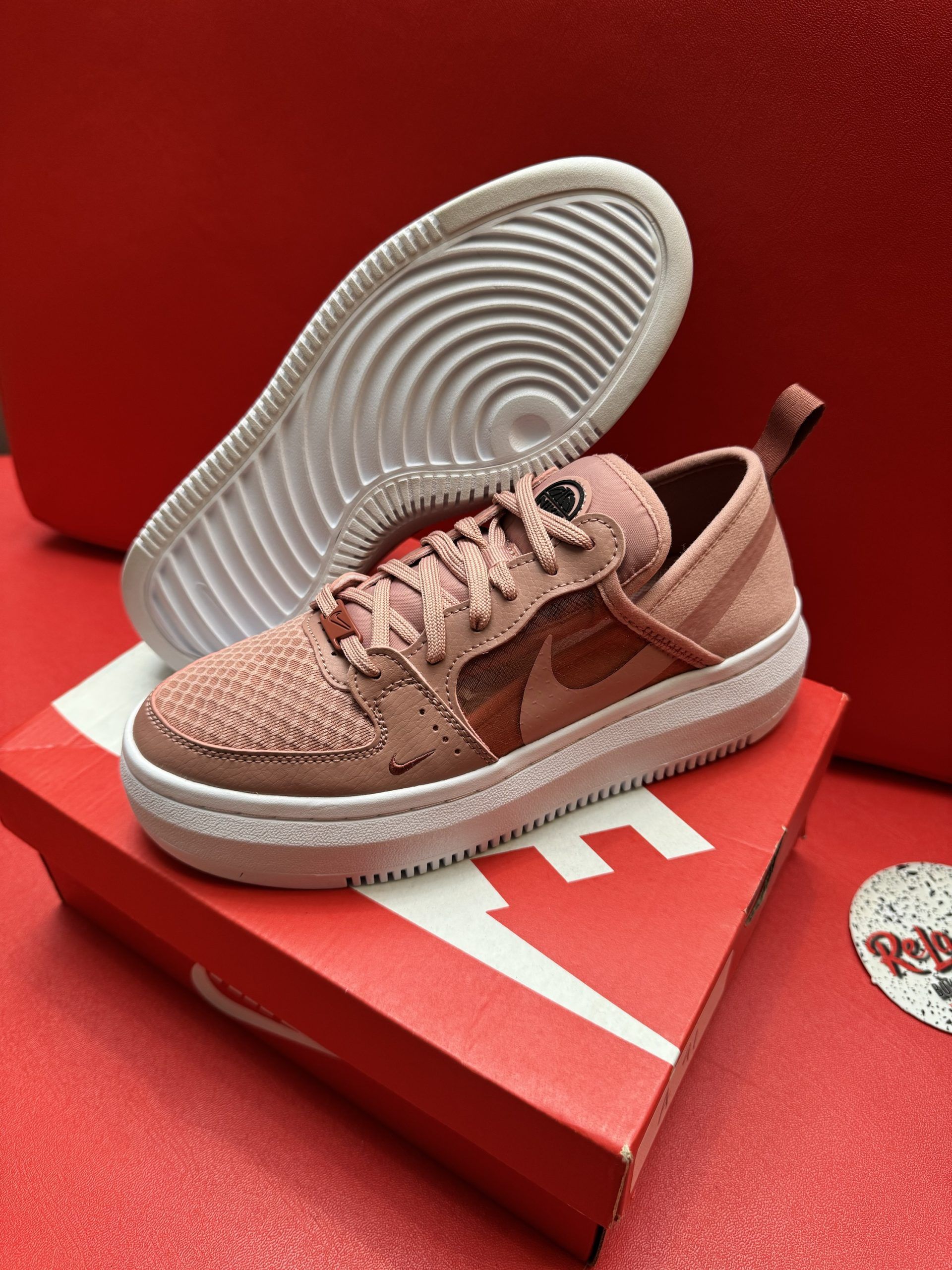 Pink Nike sneakers on a red Nike box with a white sole, set against a red background.