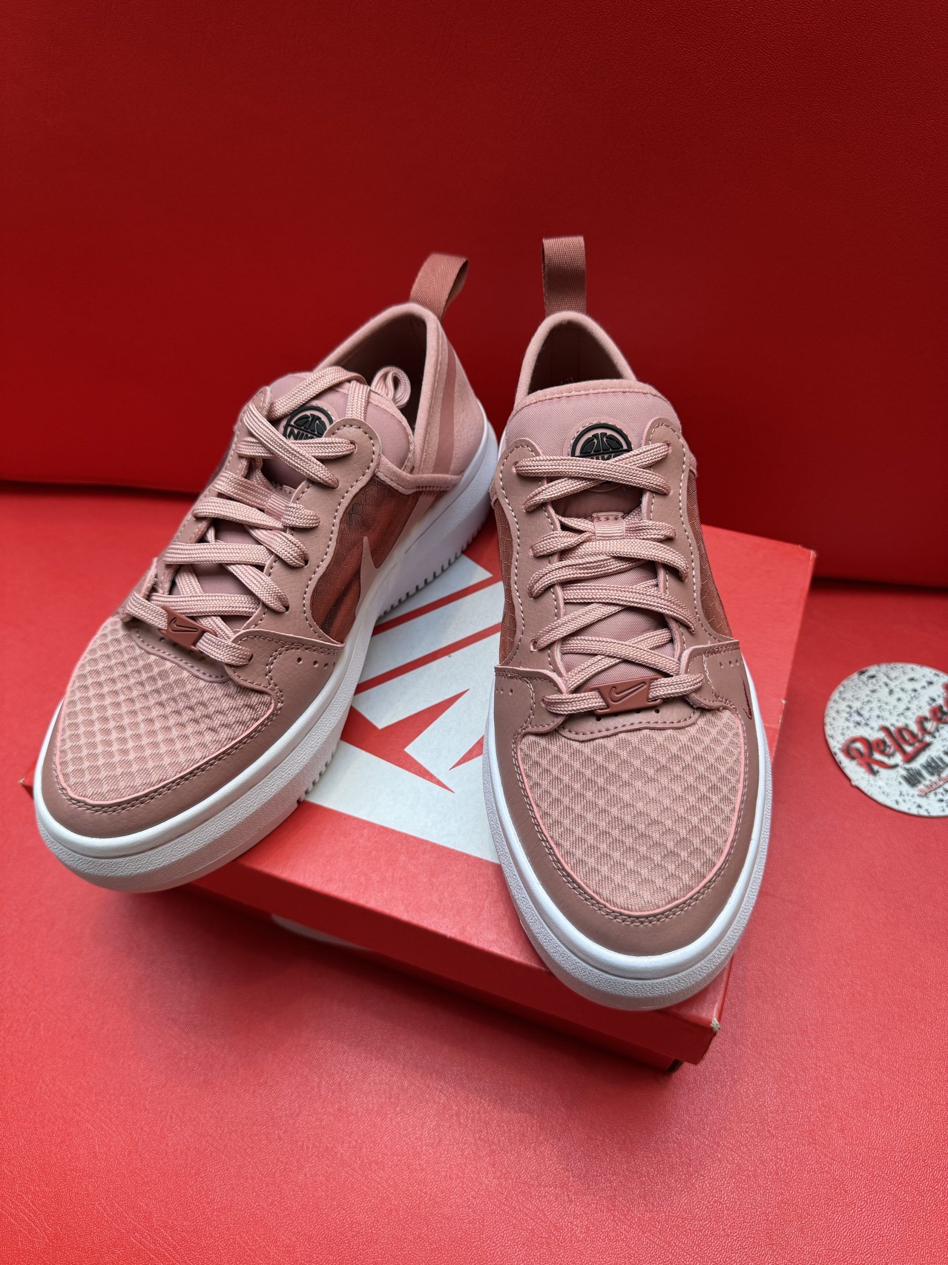Pink Nike sneakers on a red Nike box with a white sole, set against a red background.