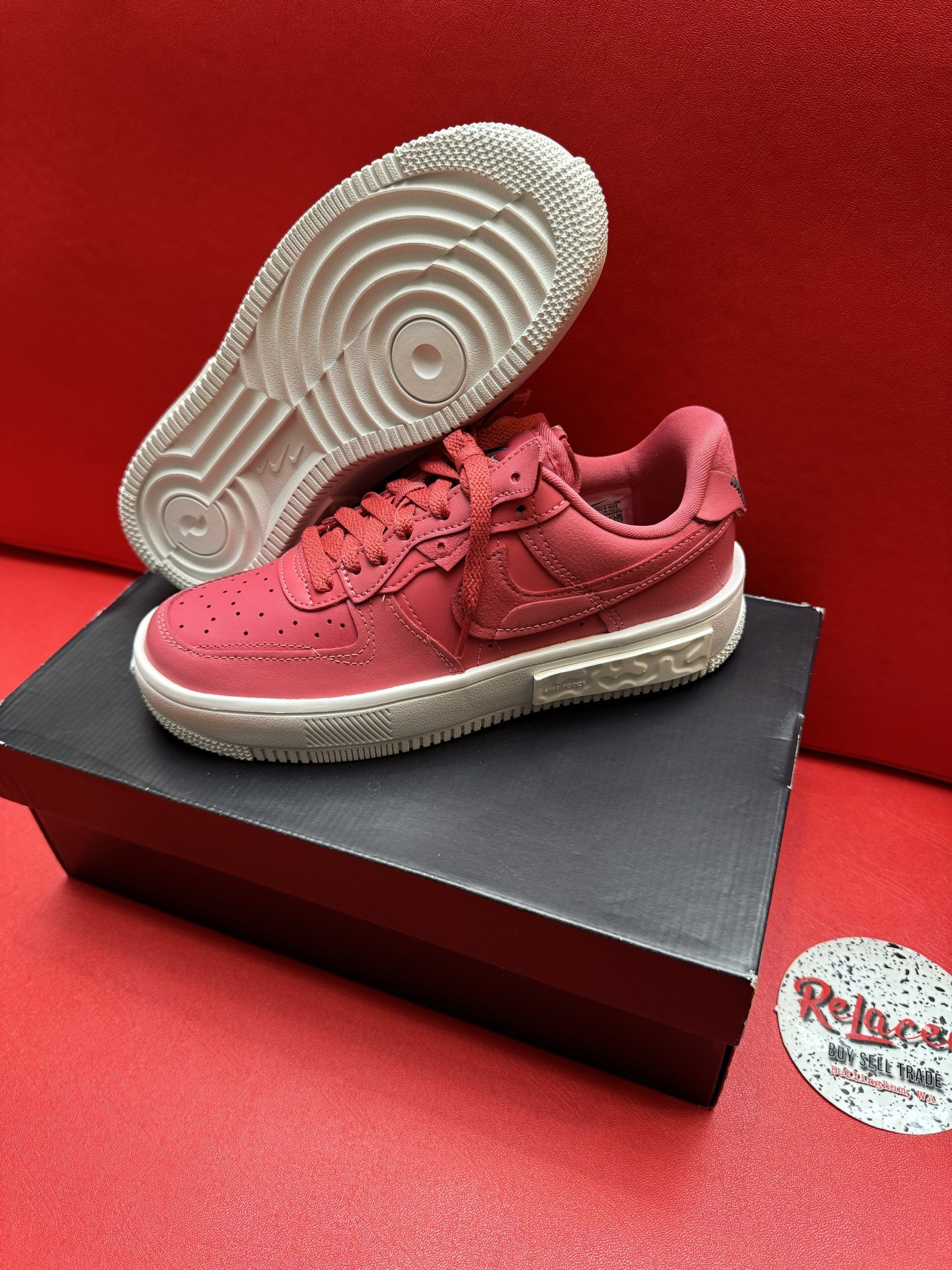 Red Nike Air Force 1 sneakers on a black box, with a white sole, and a red background.