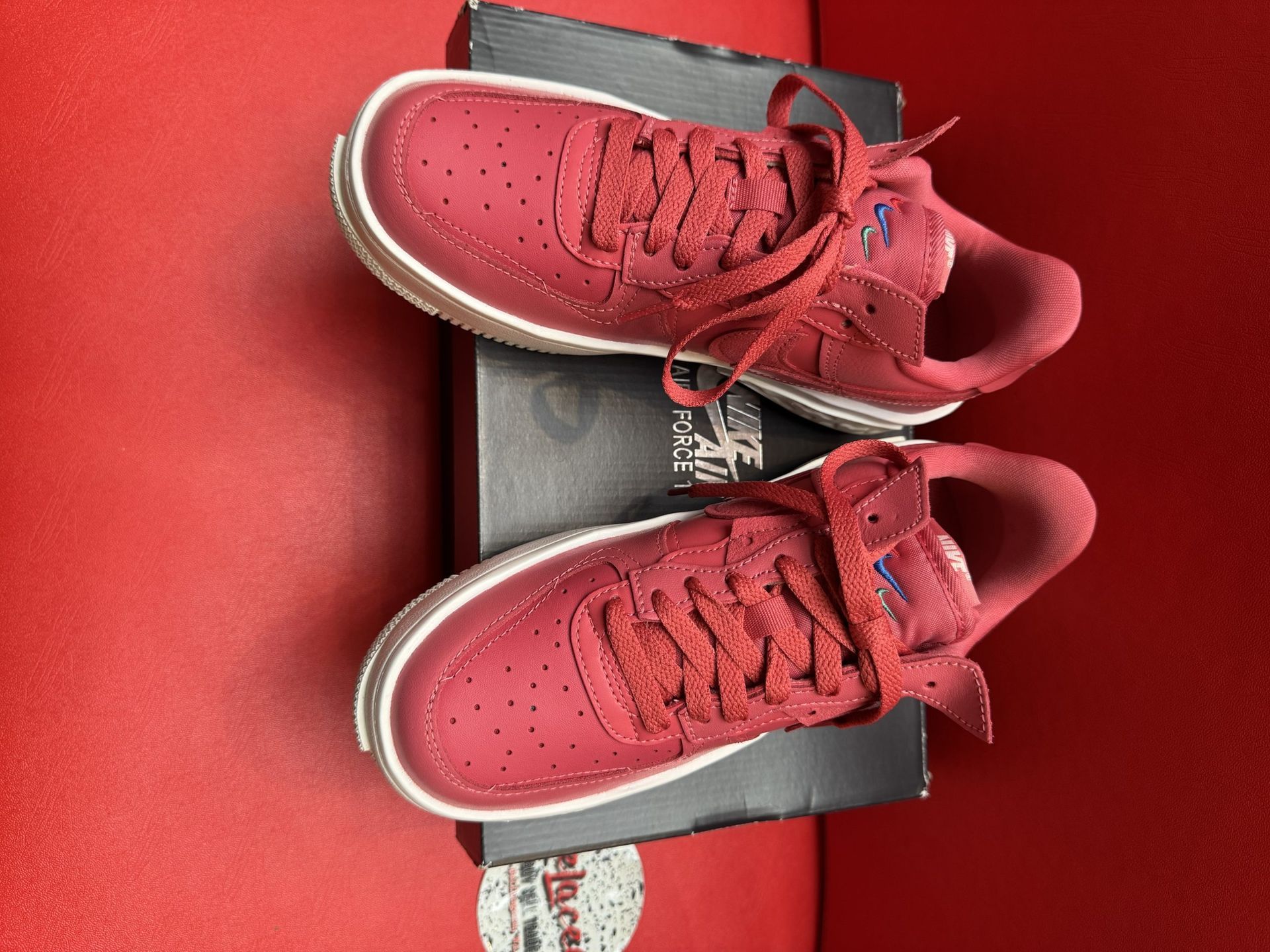 Red Nike Air Force 1 sneakers on a black box, with a white sole, and a red background.