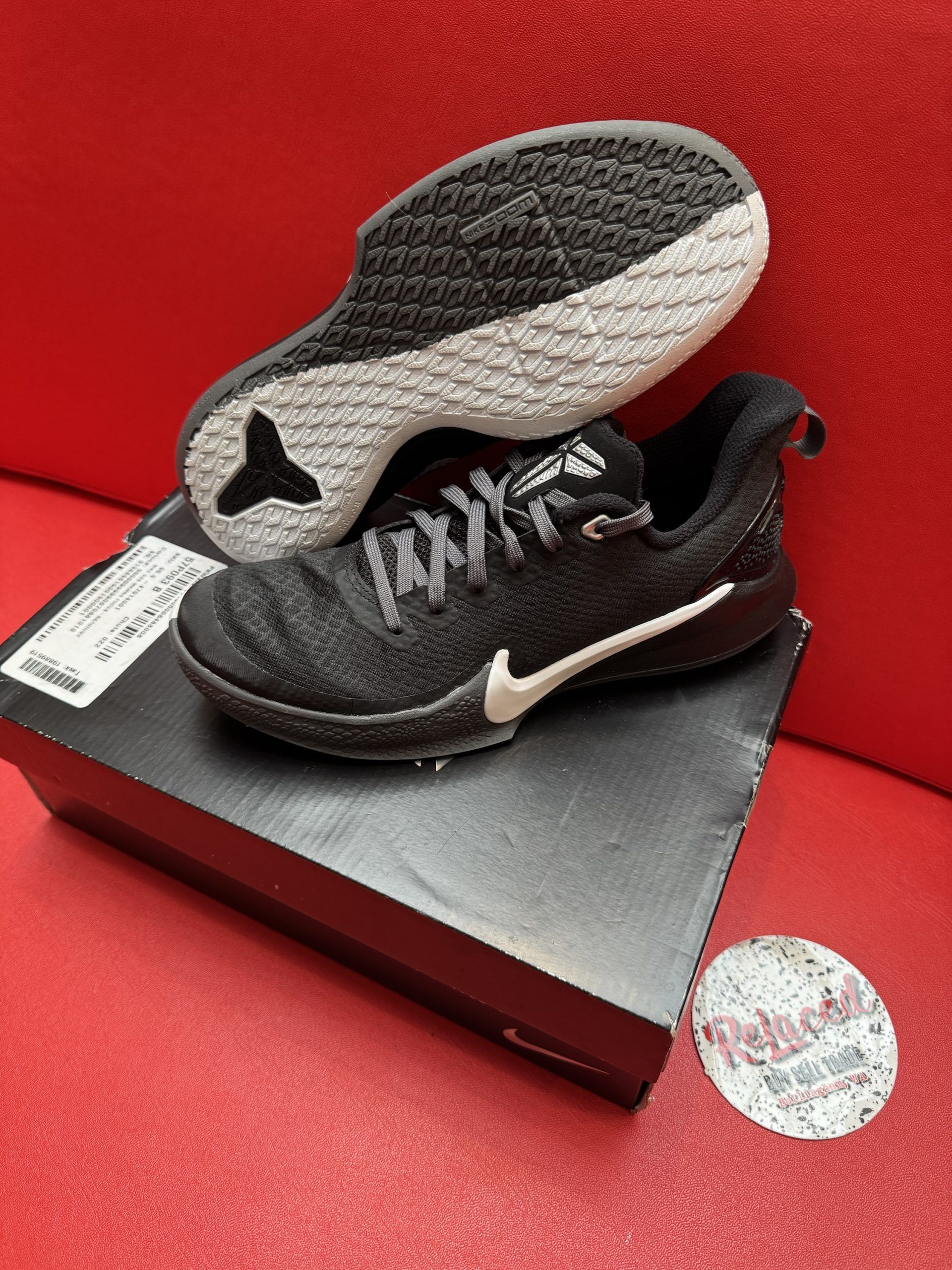 Black Nike sneakers with white swoosh, on a box, with sole visible.