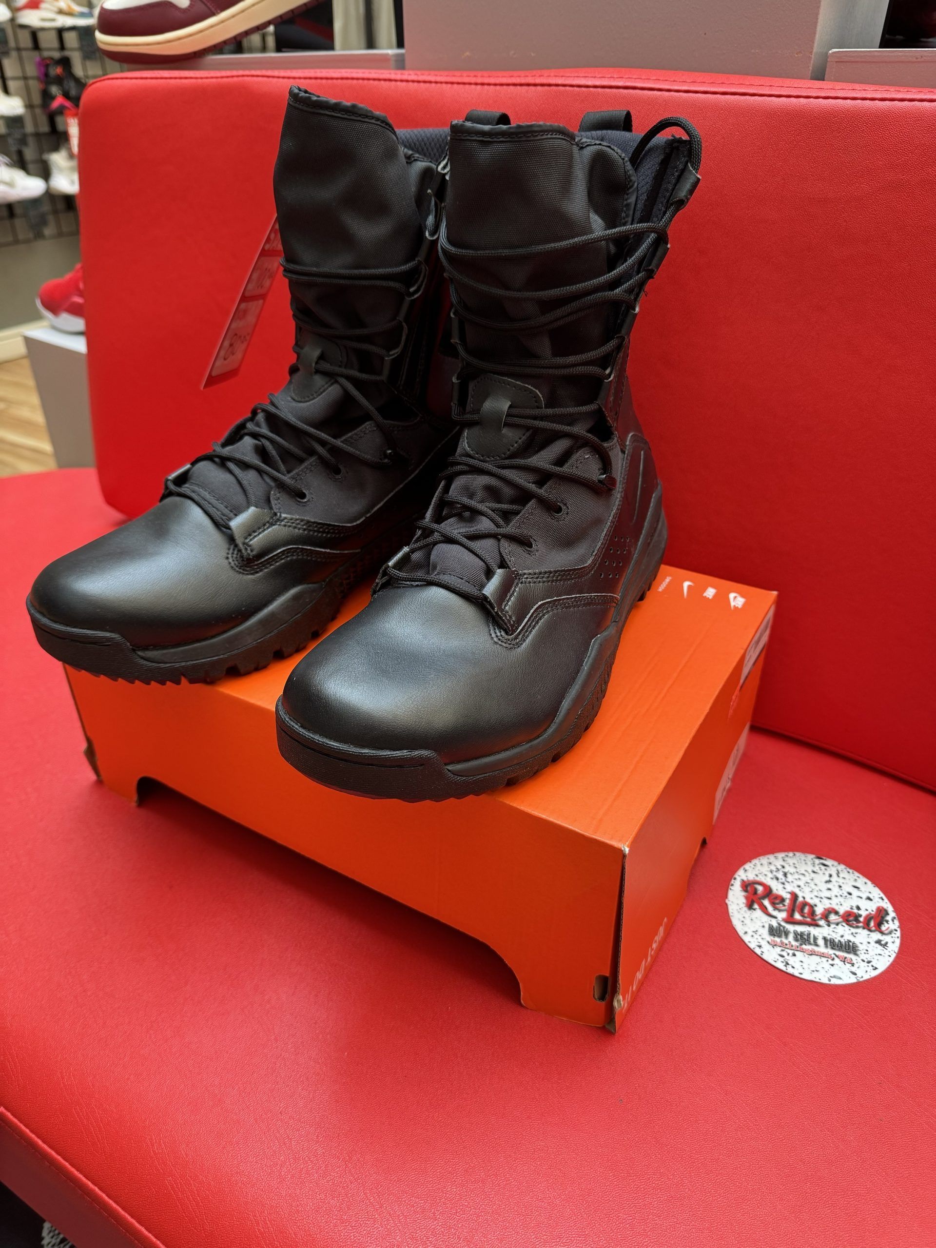 Black Nike boots on an orange shoe box, resting on a red surface.