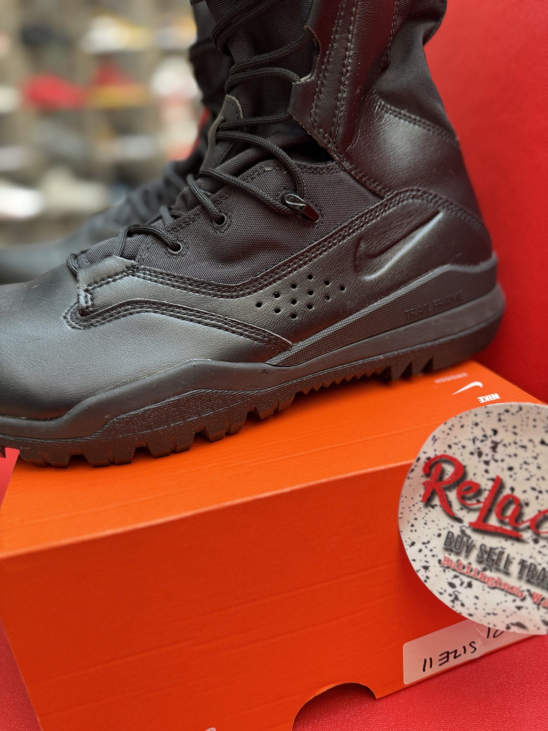 Black Nike boots on an orange shoe box, resting on a red surface.