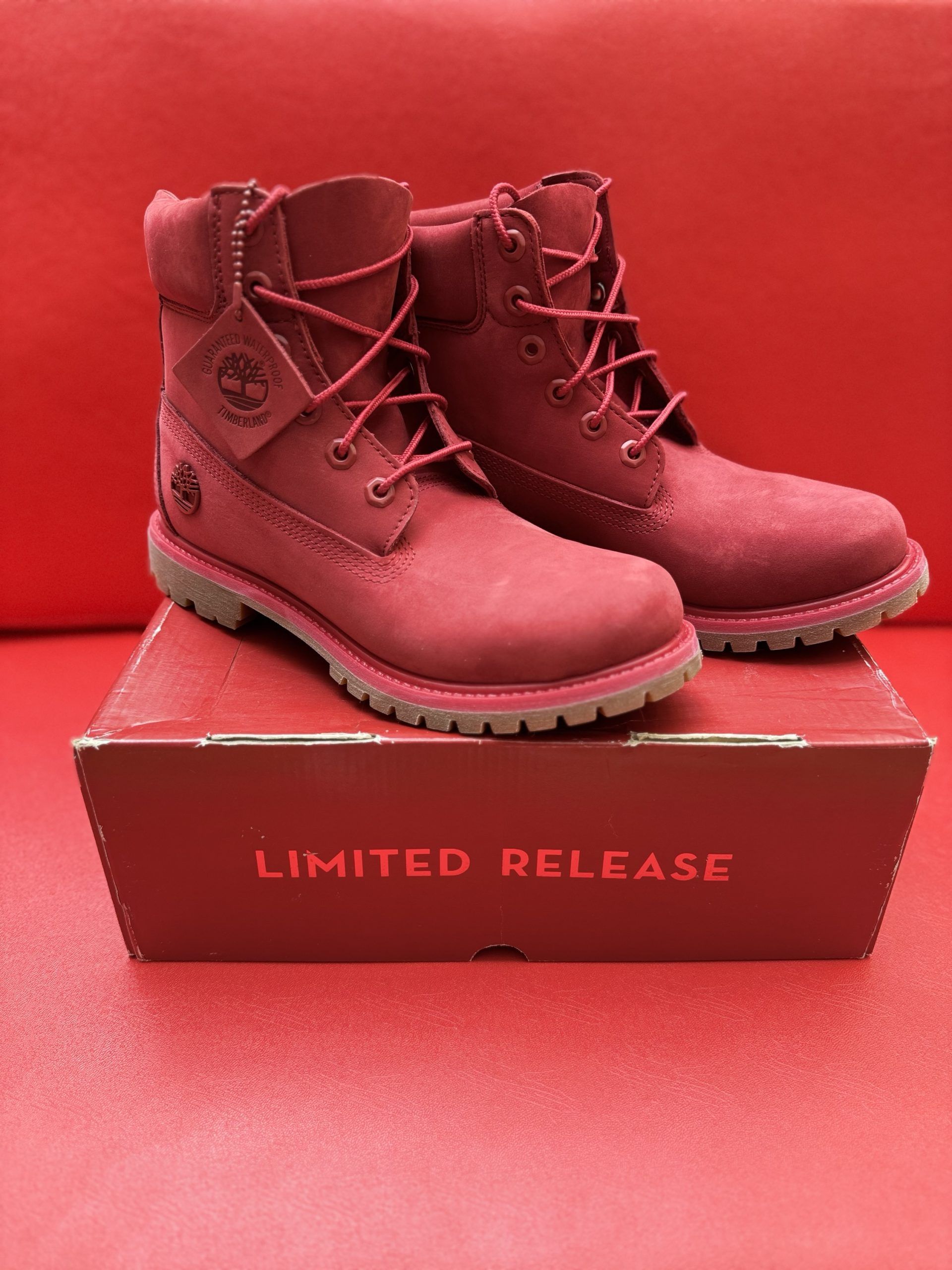 Red Timberland boots with the box on a red surface.