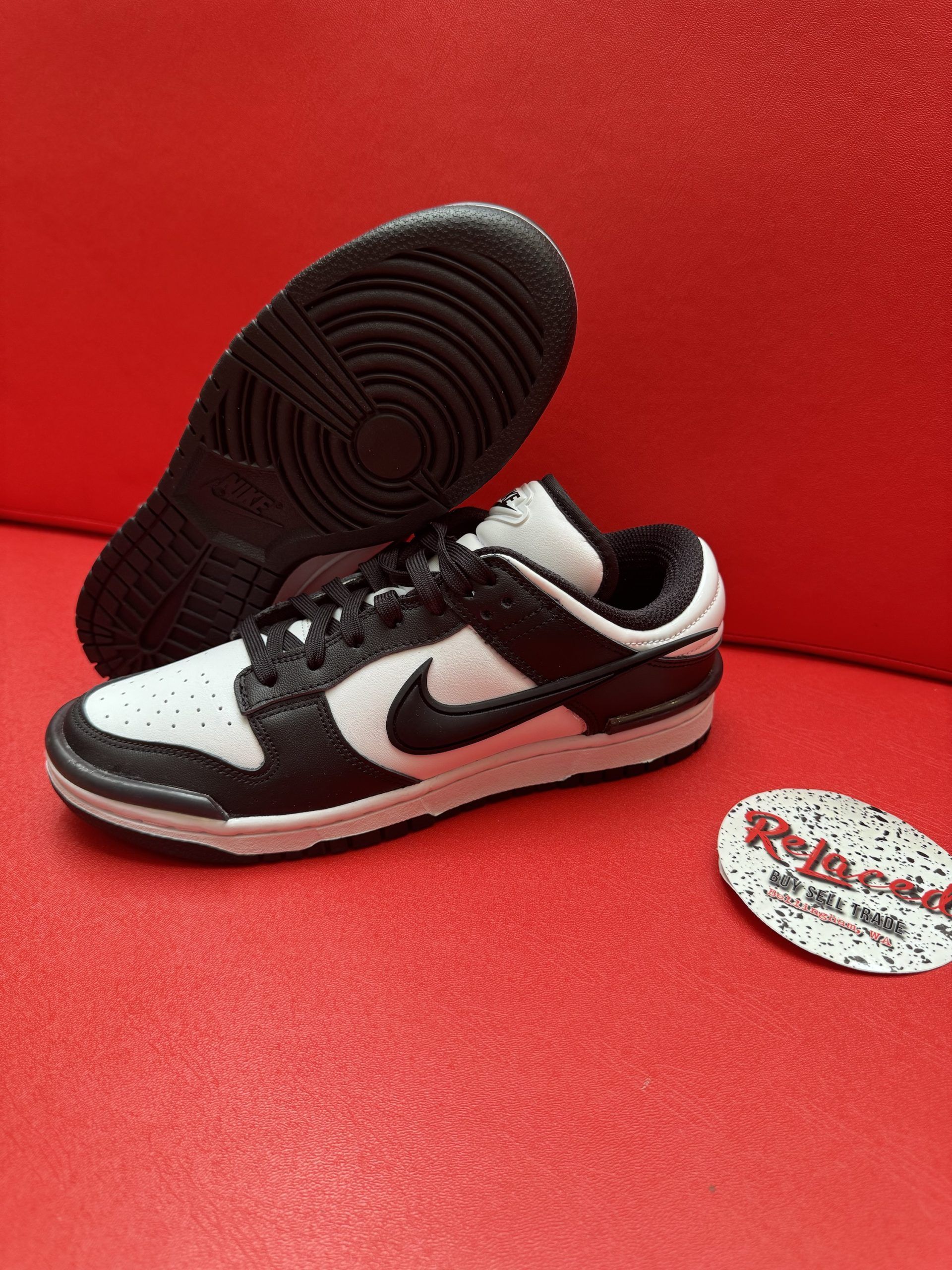 Black and white Nike Dunk Low sneaker with black sole on a red surface.
