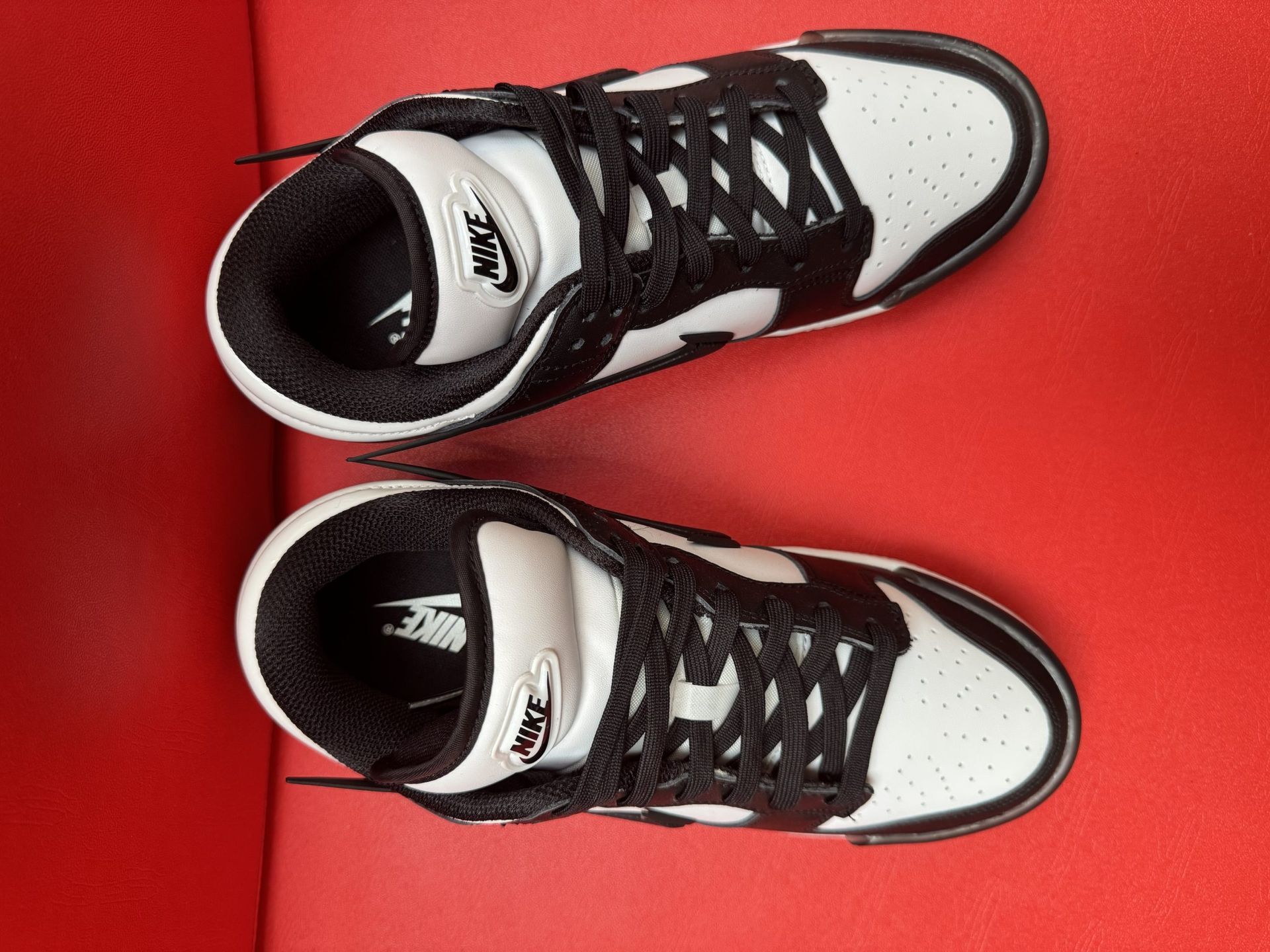 Black and white Nike Dunk Low sneaker with black sole on a red surface.