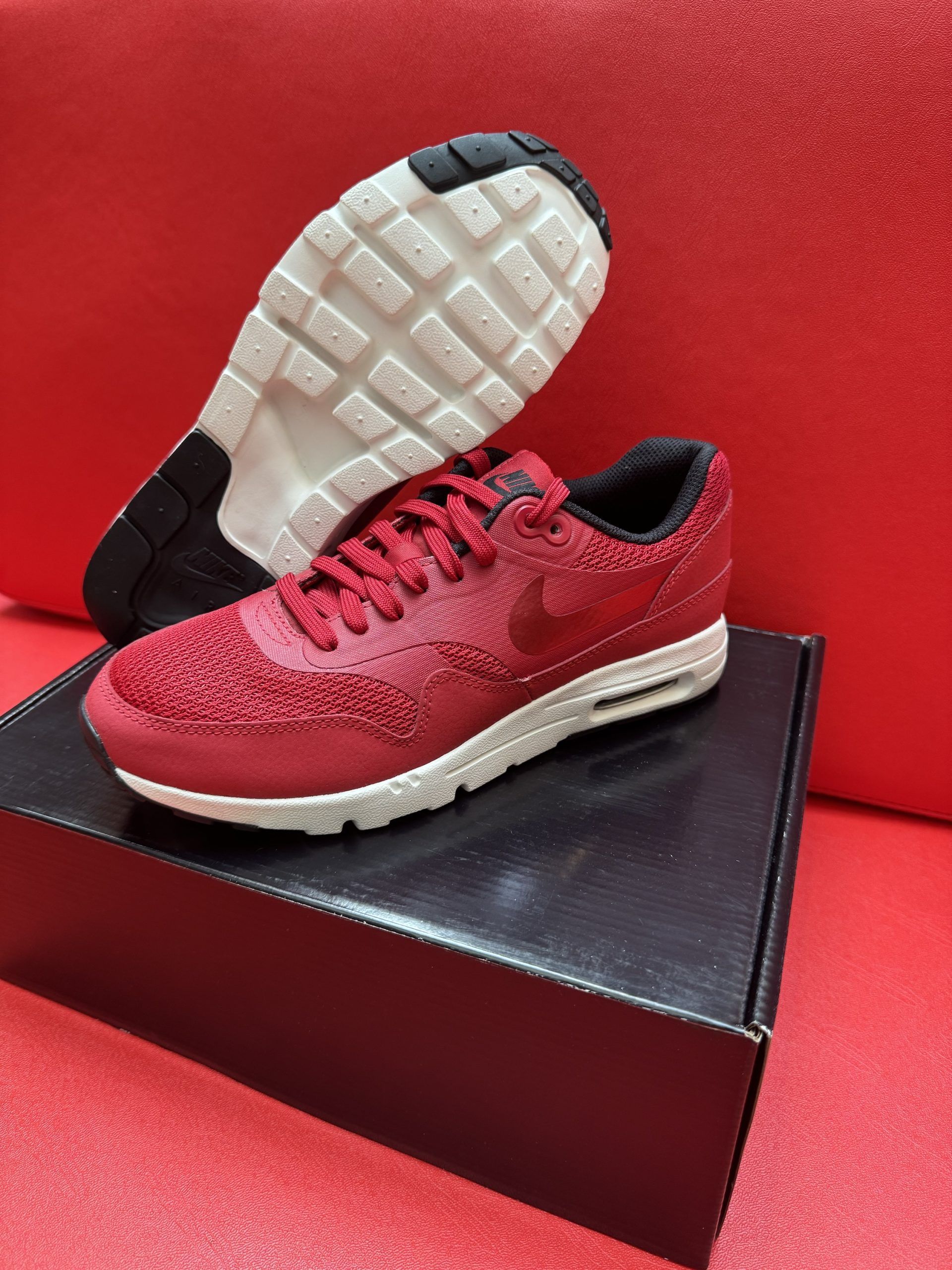 Red Nike Air Max 1 sneaker on black box, other sole visible.