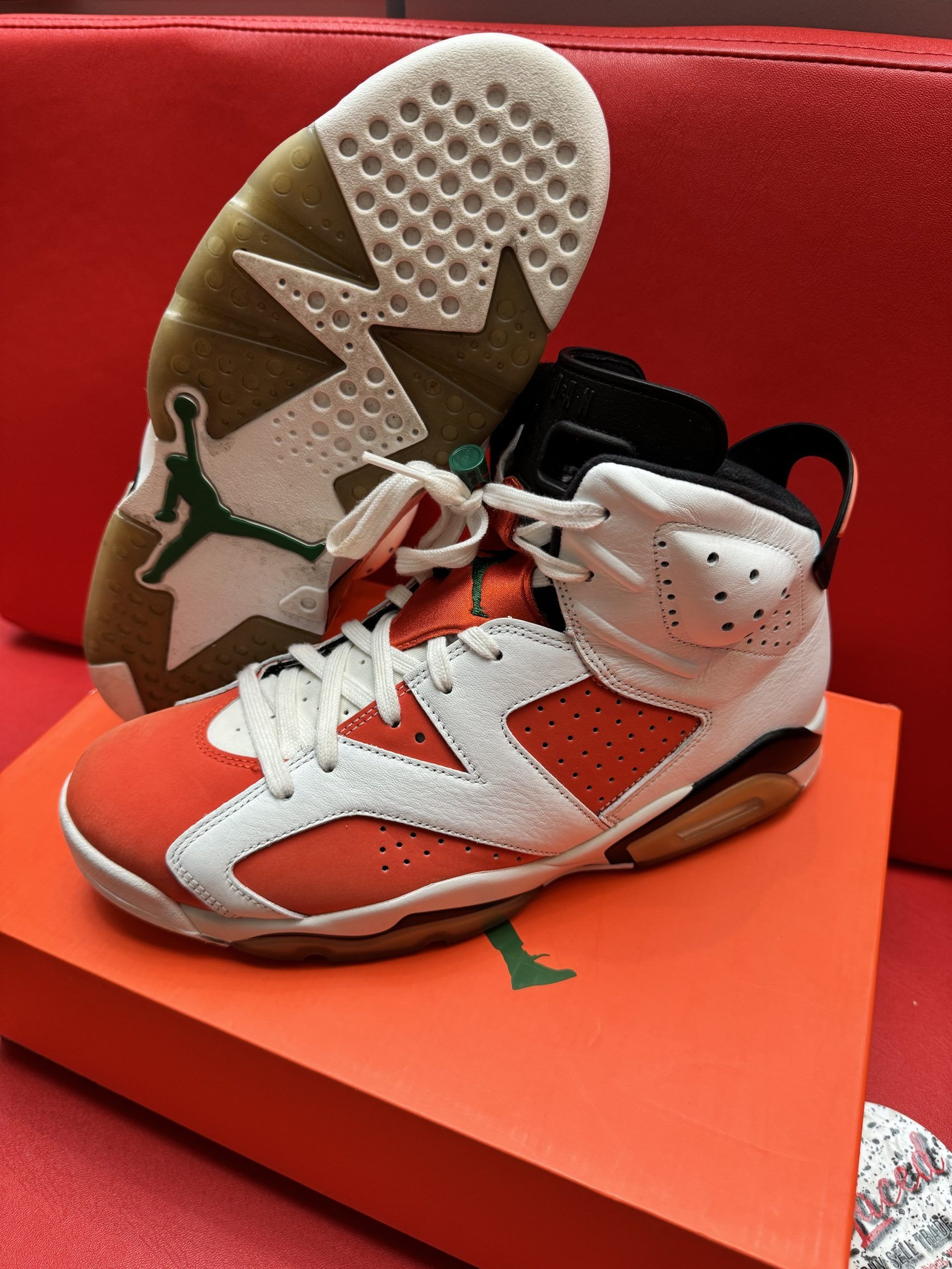 Air Jordan 6 sneakers in orange, white, and black on an orange box. One shoe is upside down, revealing the sole.