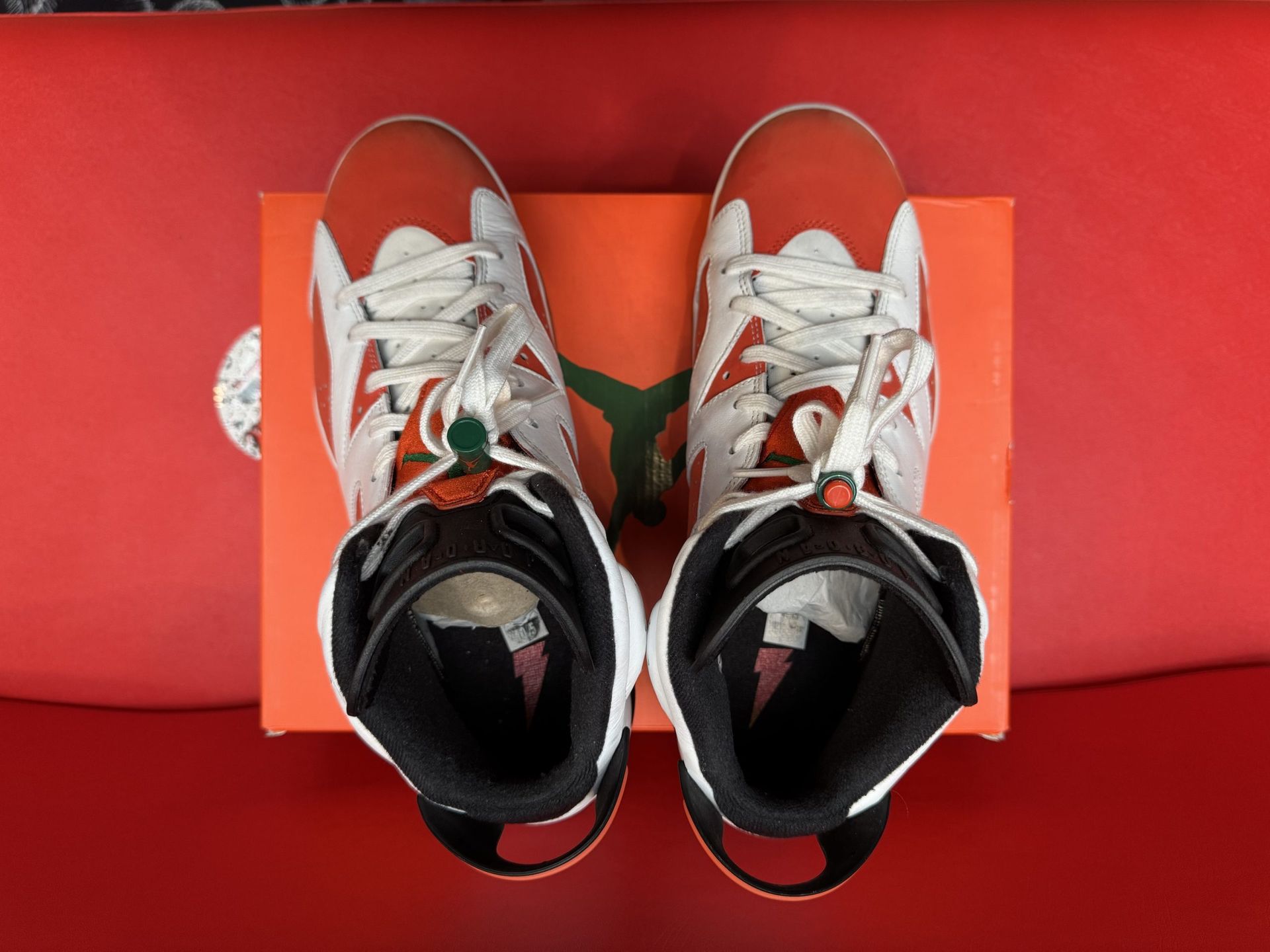 Air Jordan 6 sneakers in orange, white, and black on an orange box. One shoe is upside down, revealing the sole.