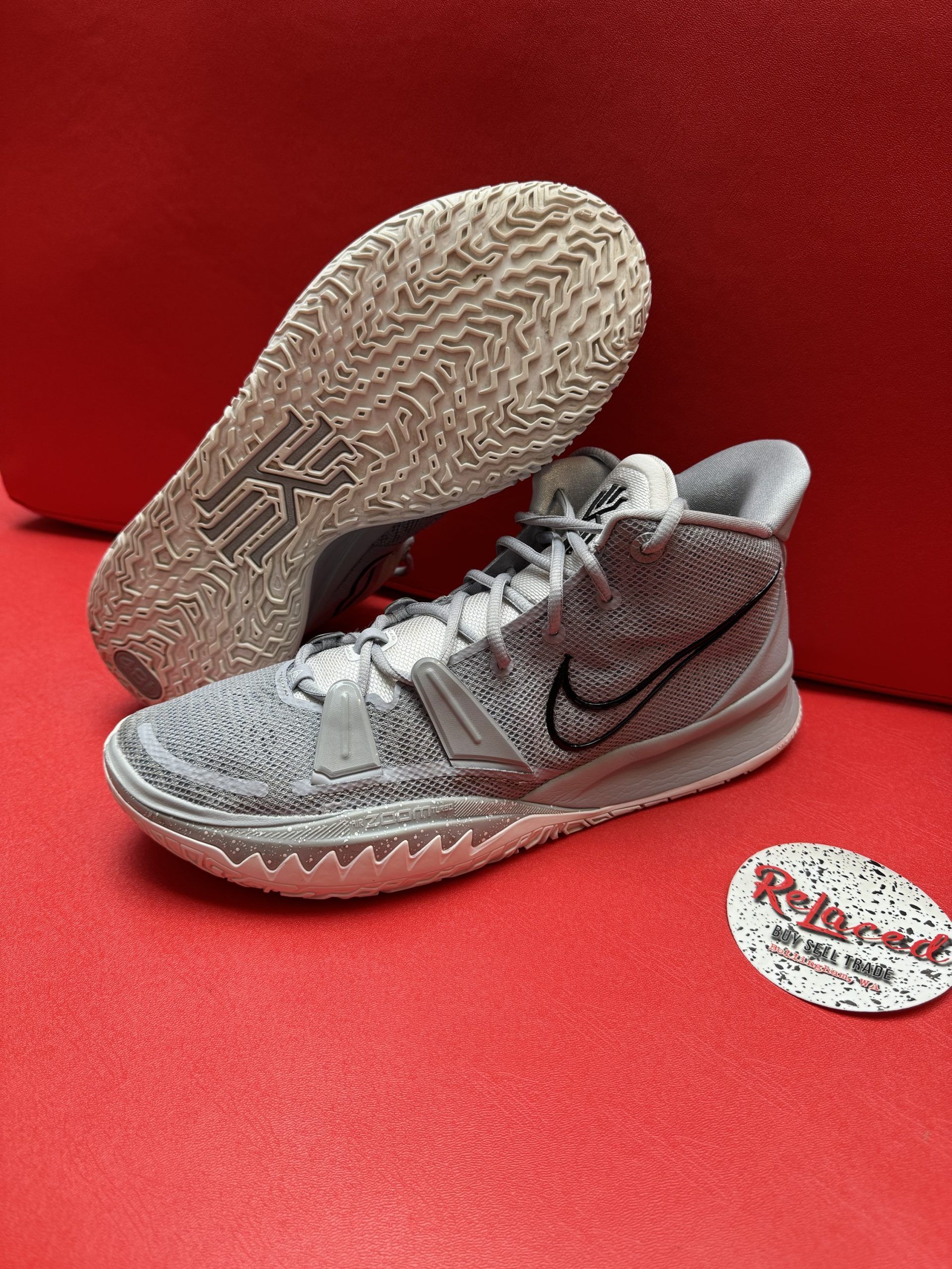Gray and white Nike Kyrie sneakers on a red surface, sole facing up. Black swoosh.
